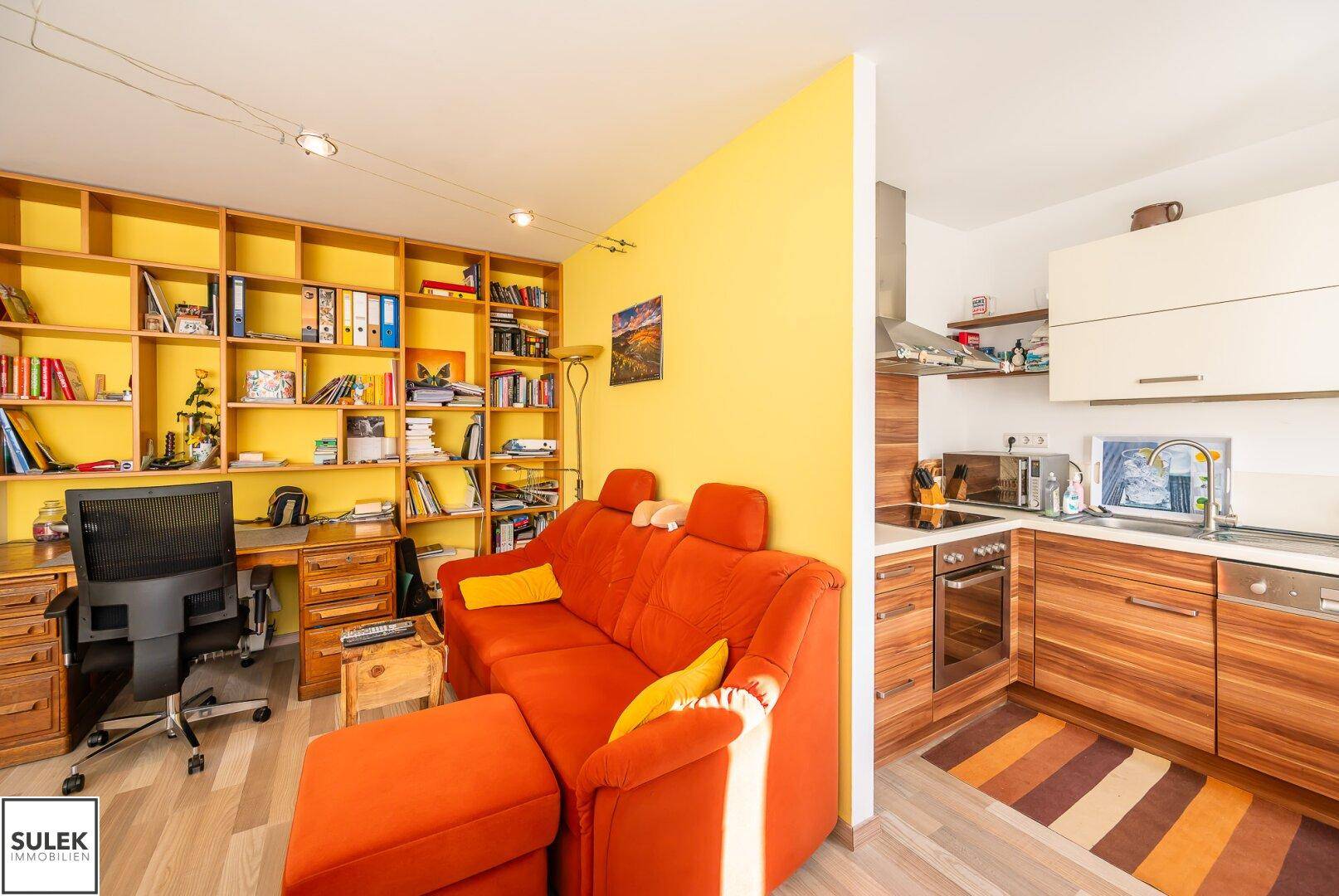 Gemütlicher Wohnbereich mit Sofa, Arbeitsplatz und angrenzender, offener Küche.