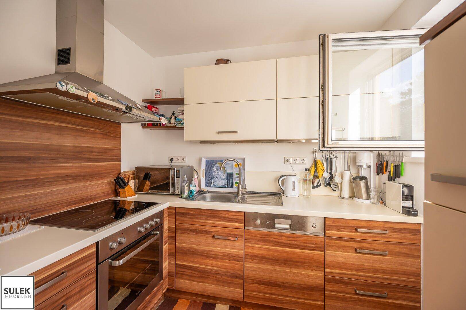 Funktionale Küche mit Holzfronten, hellen Arbeitsplatten und modernen Geräten.