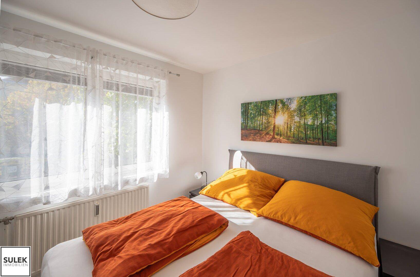 Helles Schlafzimmer mit großem Fenster, Doppelbett und Blick ins Grüne.