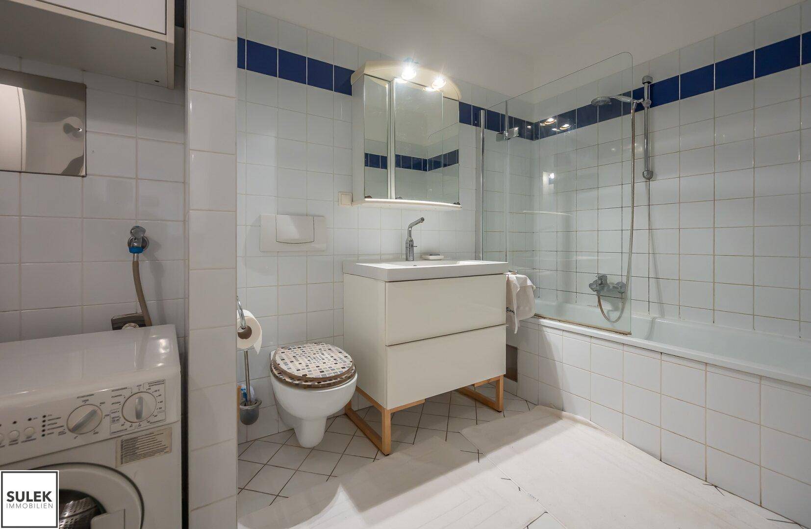 Gefliestes Badezimmer mit Badewanne, Dusche und integrierter Waschmaschine.