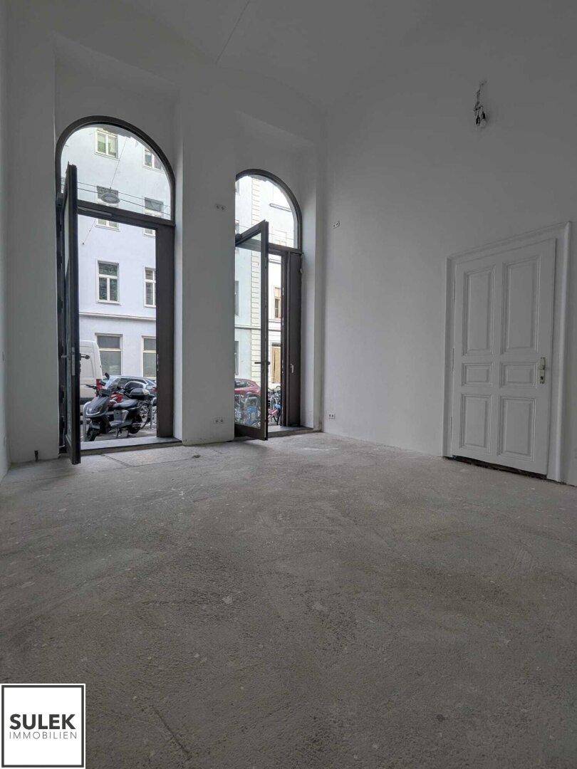 Geräumiger, heller Innenraum mit hohen Decken und großen Rundbogenfenstern mit Blick auf die Straße.