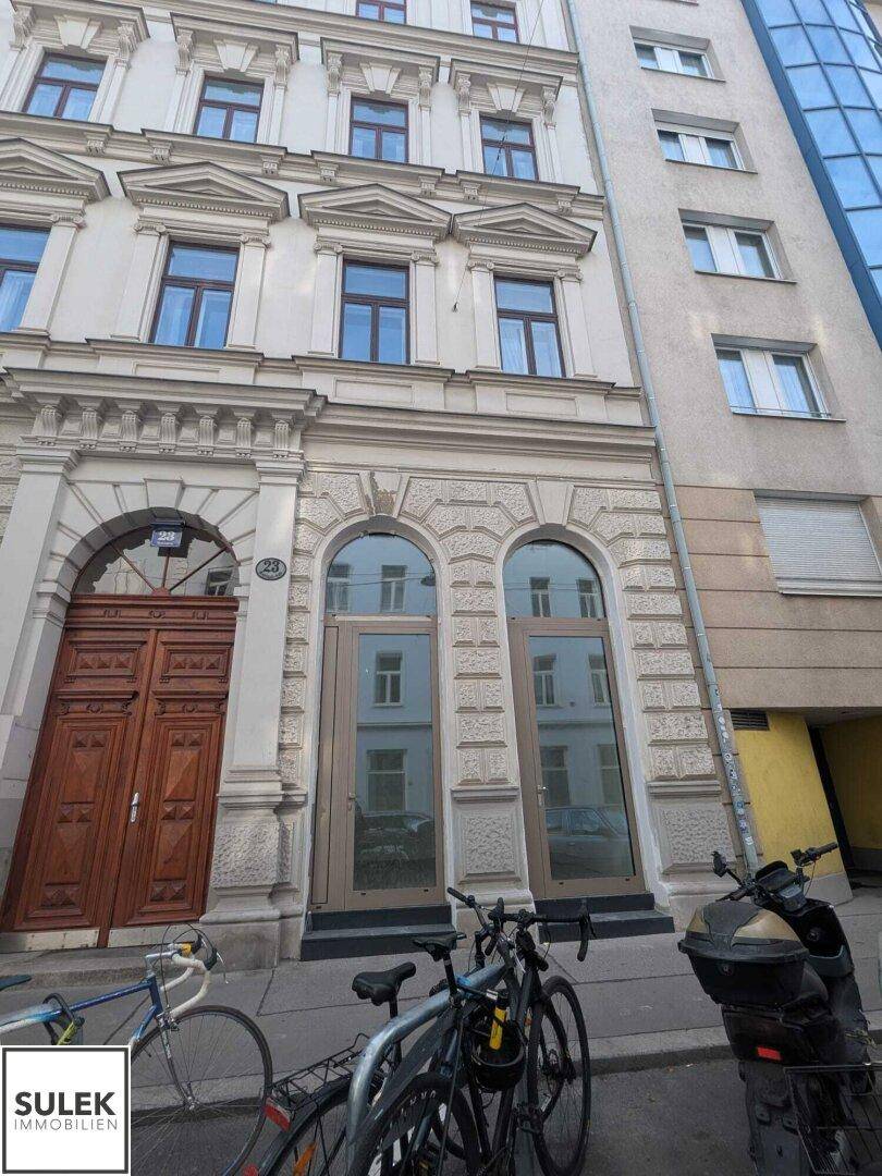 Historische Fassade eines Gebäudes mit verzierten Fenstern und einem großen Holztor im Erdgeschoss.
