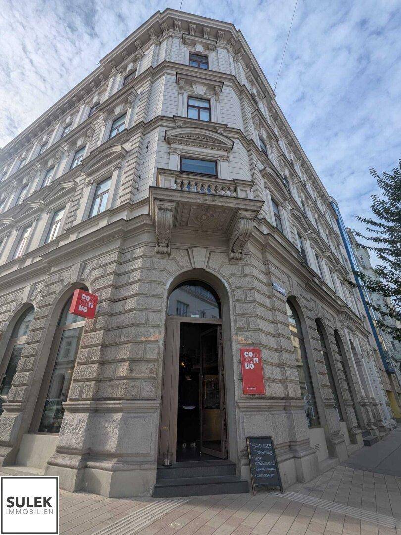 Eindrucksvolle Eckfassade eines historischen Gebäudes mit reich verzierten Details und einem kleinen Balkon.
