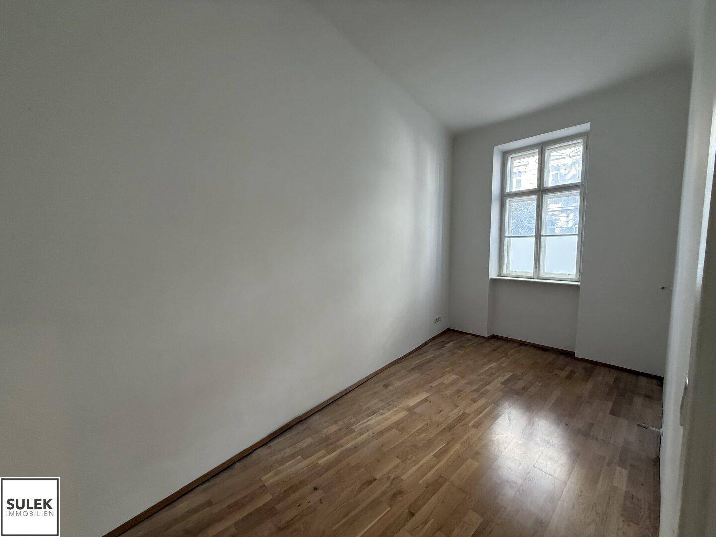 Ruhiges Zimmer mit glänzendem Holzboden und einem Fenster, das eine angenehme Atmosphäre schafft.