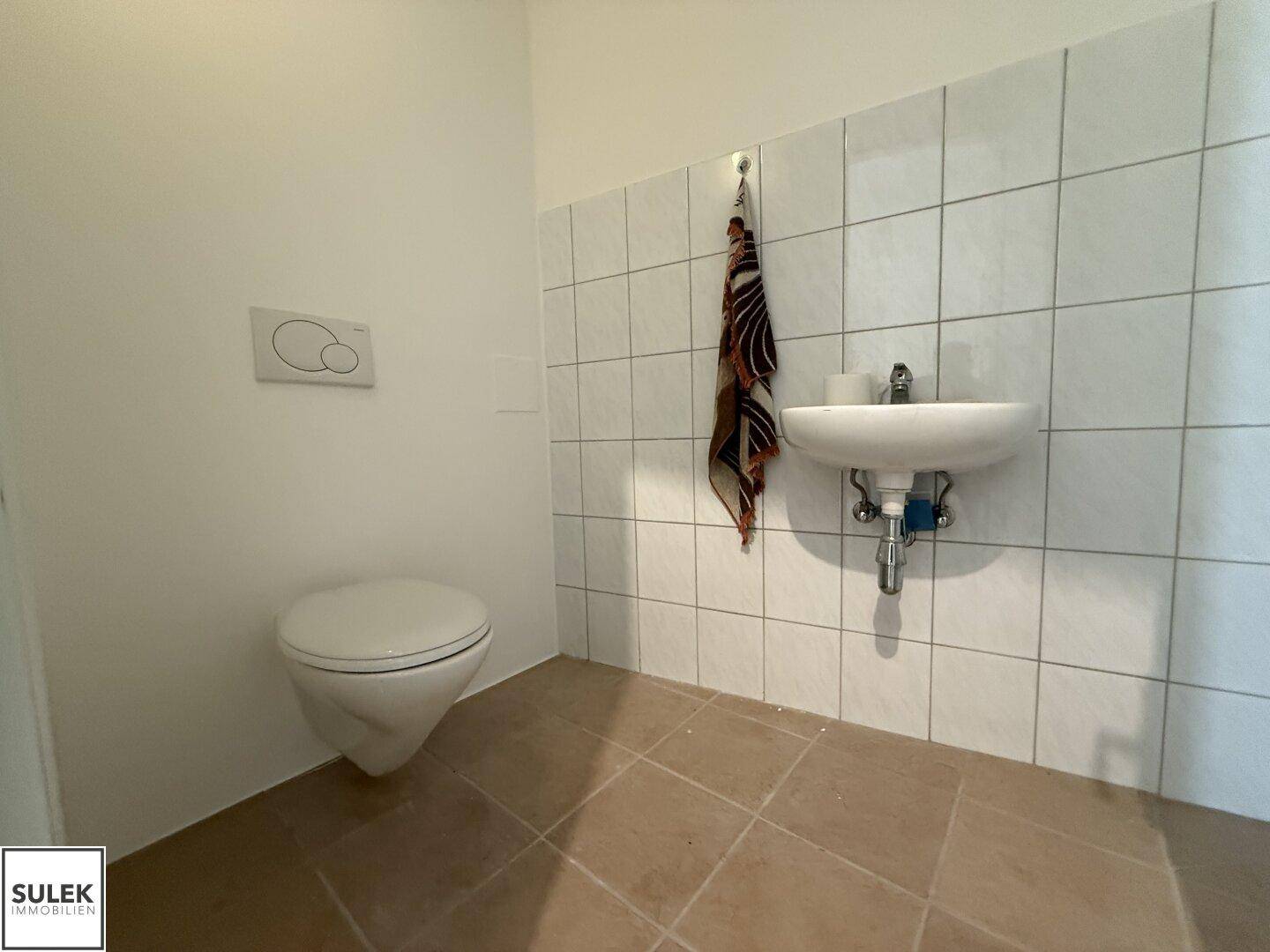 Modernes Badezimmer mit Wand-WC, Waschbecken und weißen Fliesen an den Wänden.