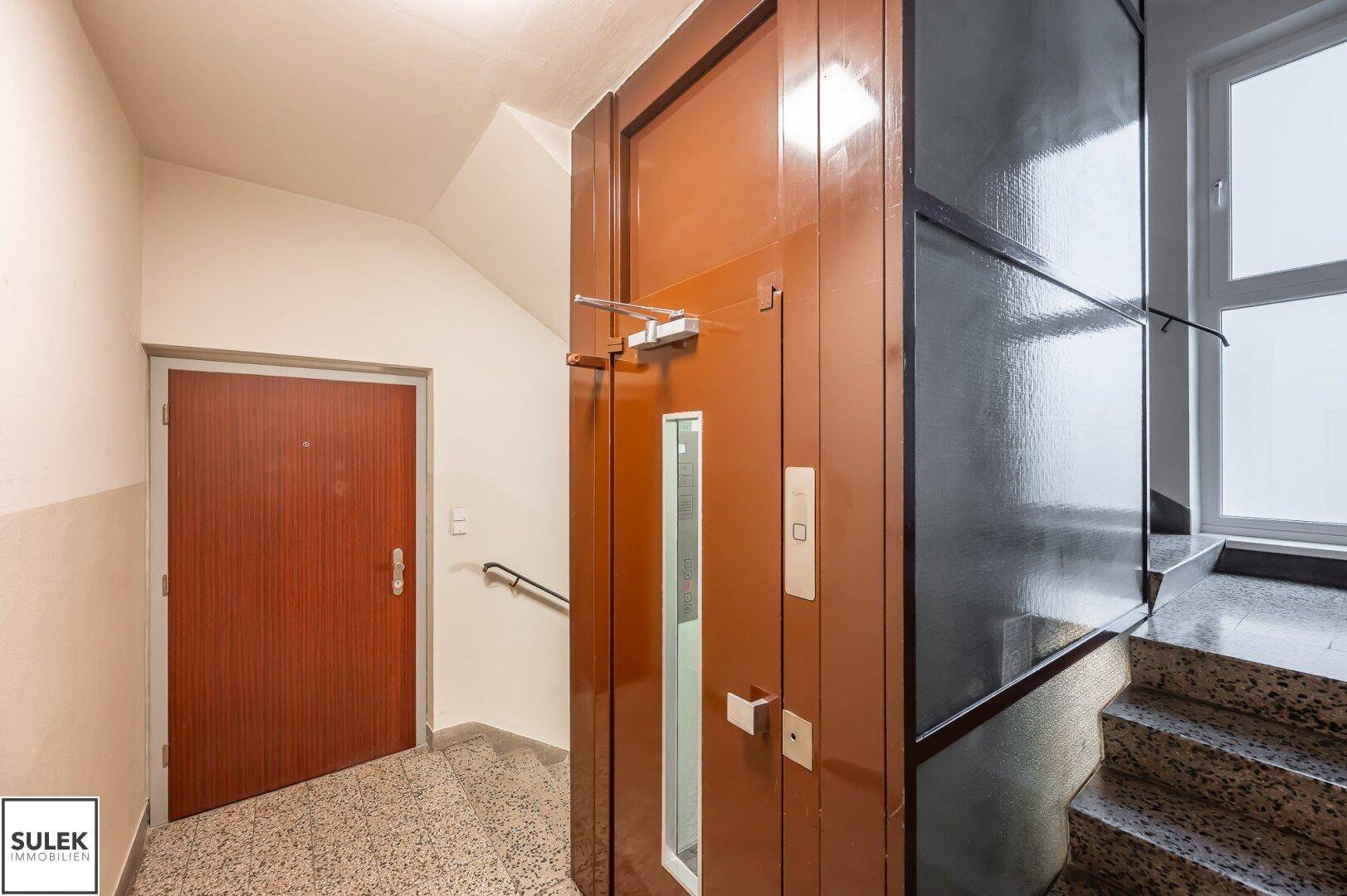 Treppenhaus mit Aufzug, Terrazzoboden und Zugang zu den oberen Etagen.