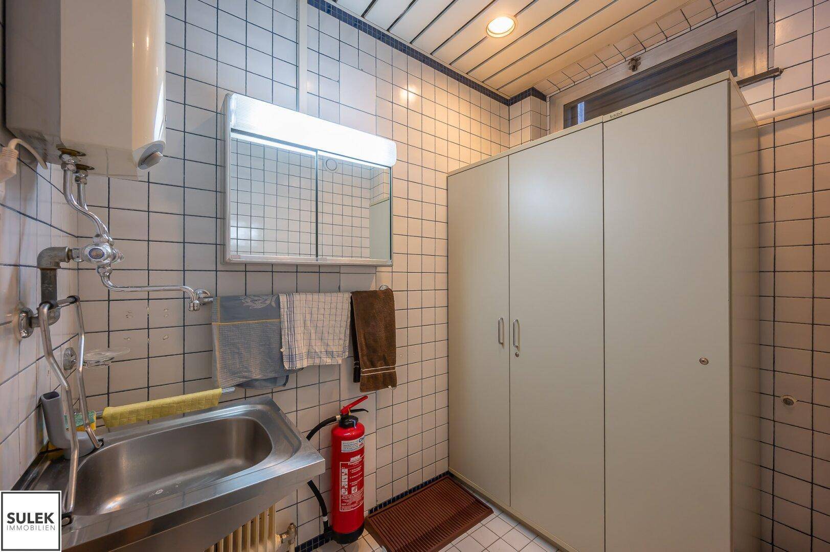 Hauswirtschaftsraum mit Waschbecken, Boiler, Schränken und Fliesenboden.
