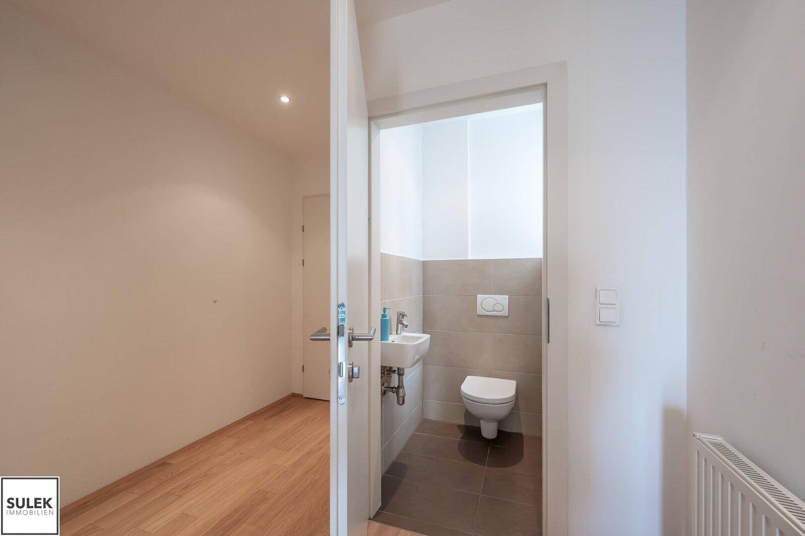 Separates Gäste-WC mit wandhängender Toilette und kleinem Waschbecken, in schlichtem Design.
