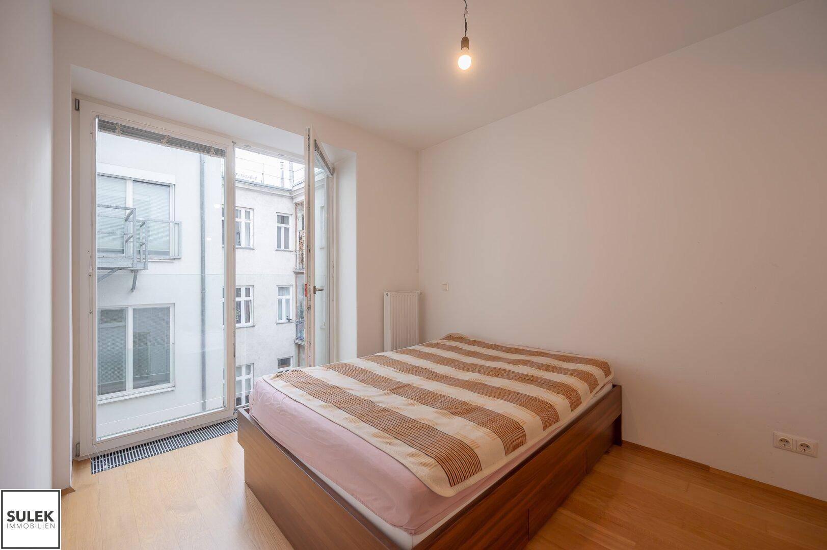 Schlafzimmer mit Holzbett und Zugang zu einem Balkon, der einen Blick auf den Innenhof bietet.