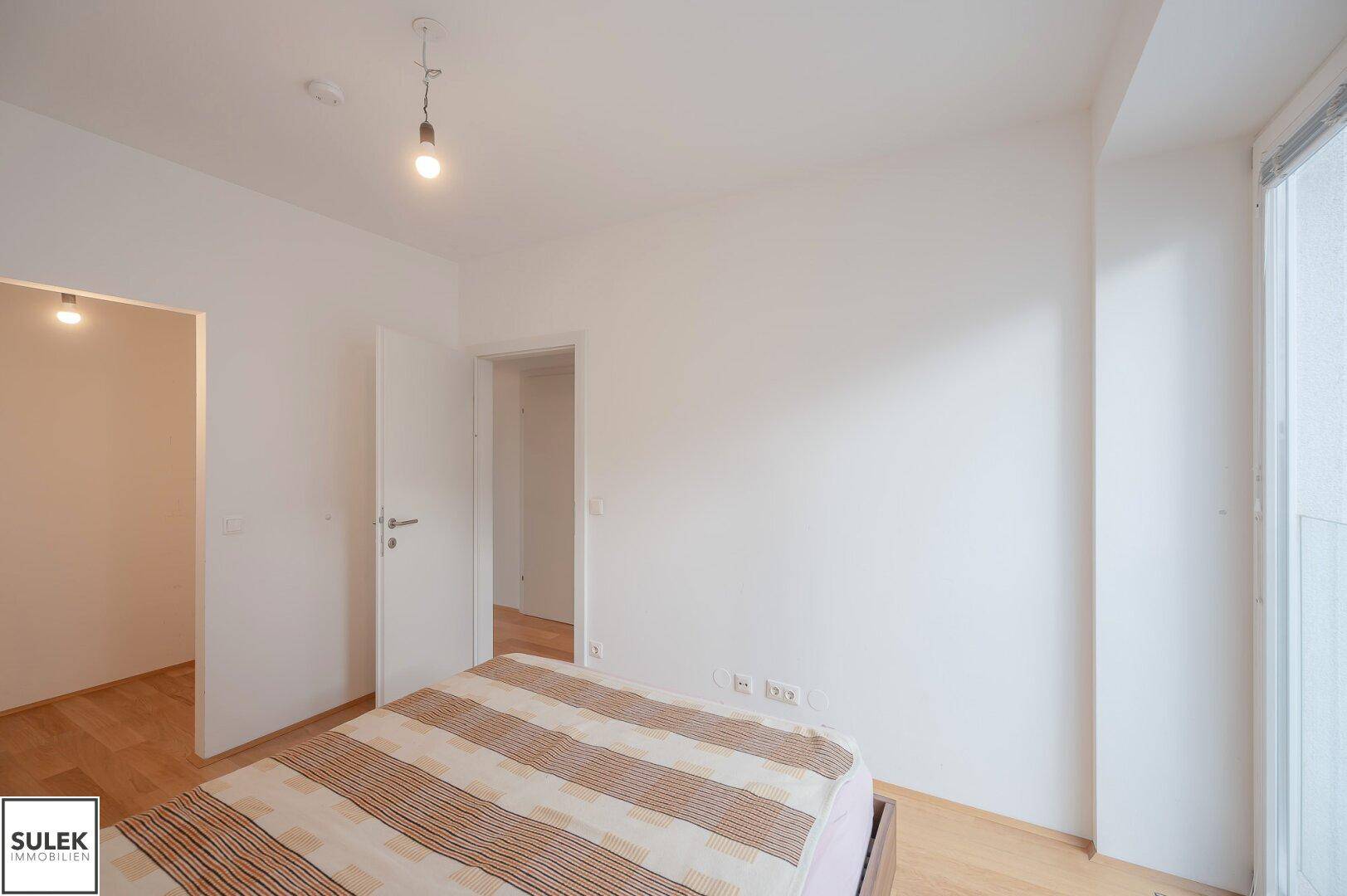 Schlafzimmer mit hellem Parkettboden und Zugang zu weiteren Räumen, in neutralen Farben gehalten.