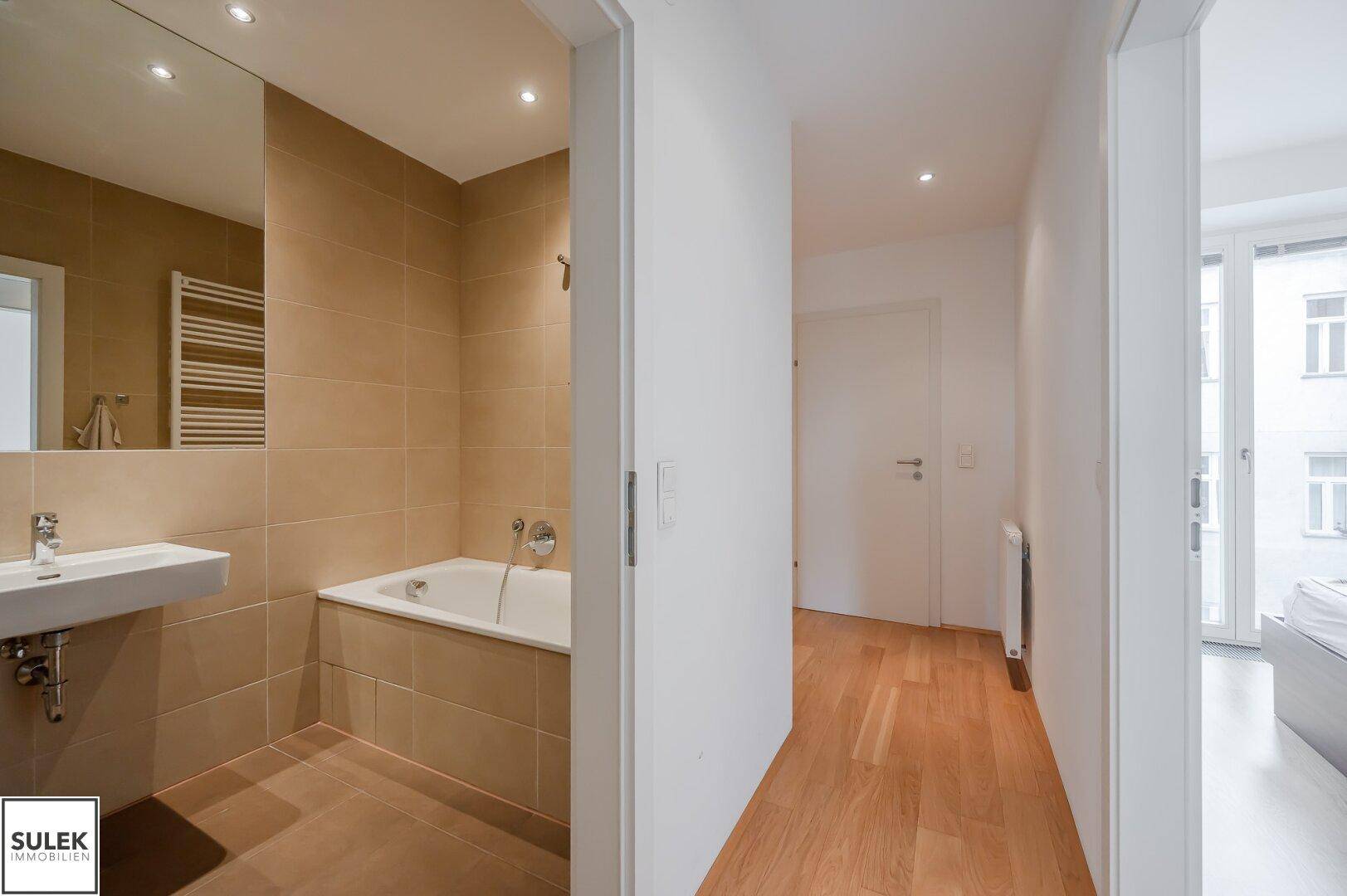 Modernes Badezimmer mit Badewanne, Waschbecken und großem Spiegel, teilweise gefliest.