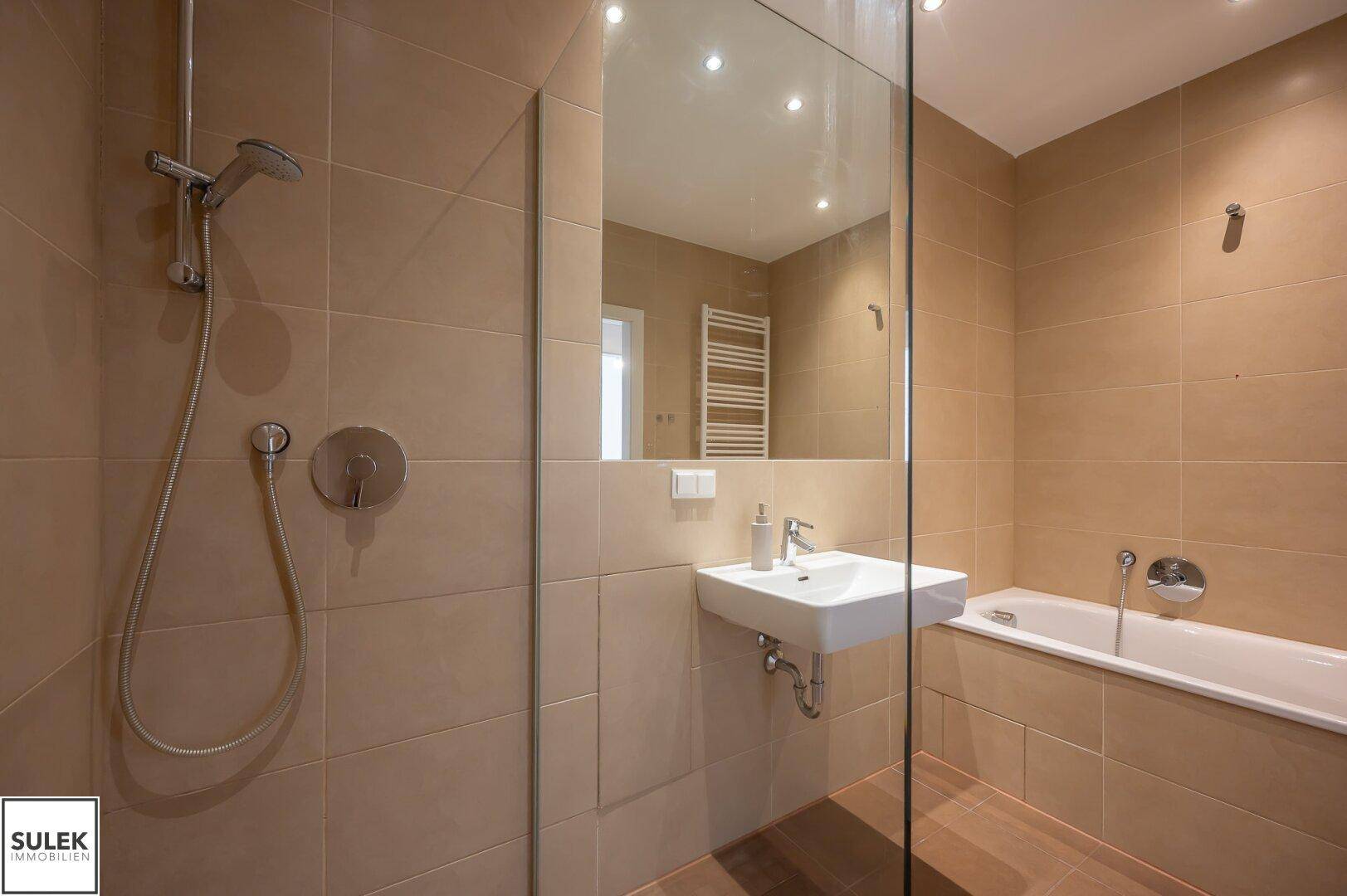 Helles Badezimmer mit Badewanne, Duschbereich und modernem Waschbecken, komplett gefliest.
