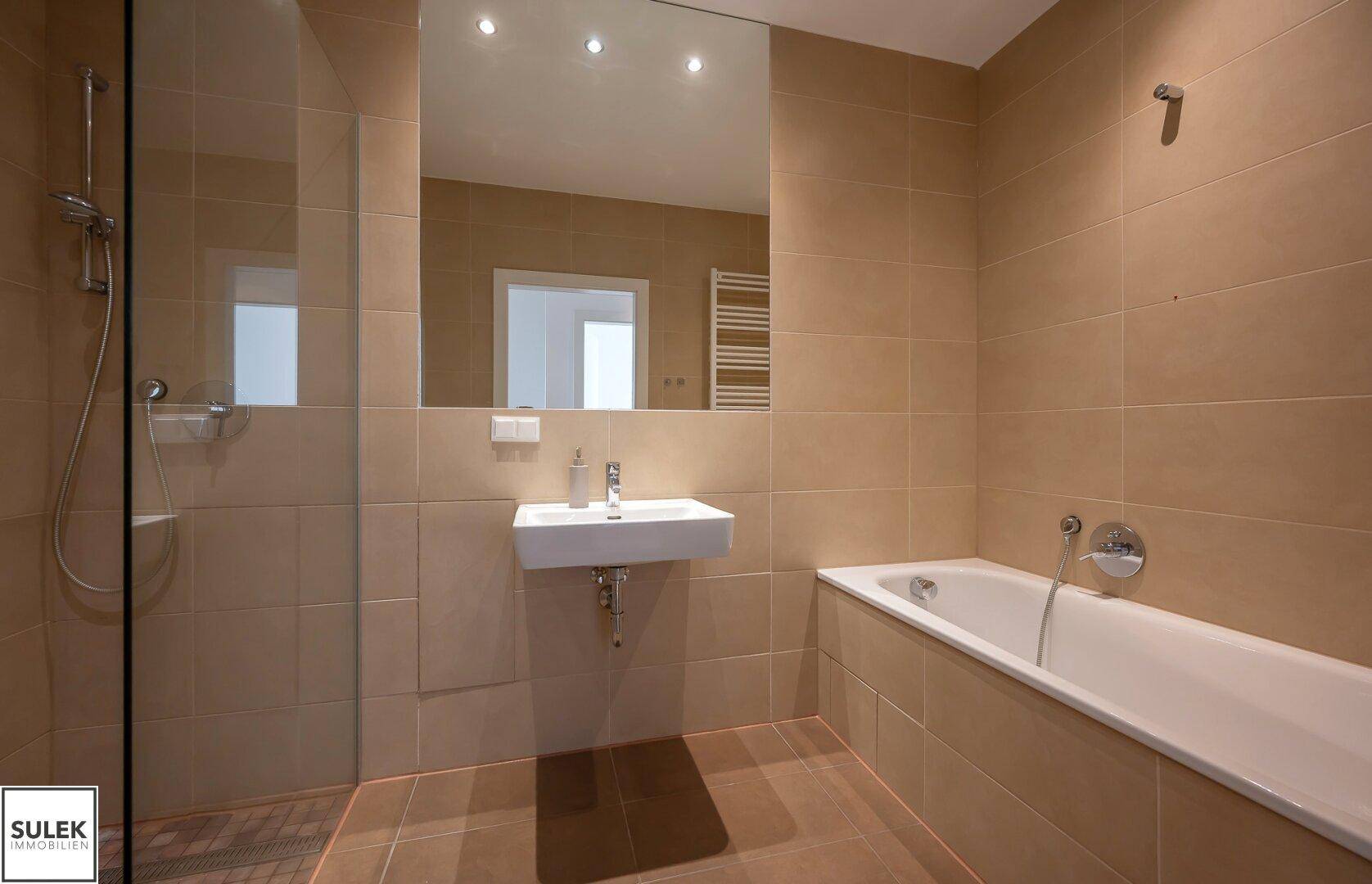 Zeitgemäßes Badezimmer mit Badewanne, Duschbereich und elegantem Waschbecken, in neutralen Farbtönen.