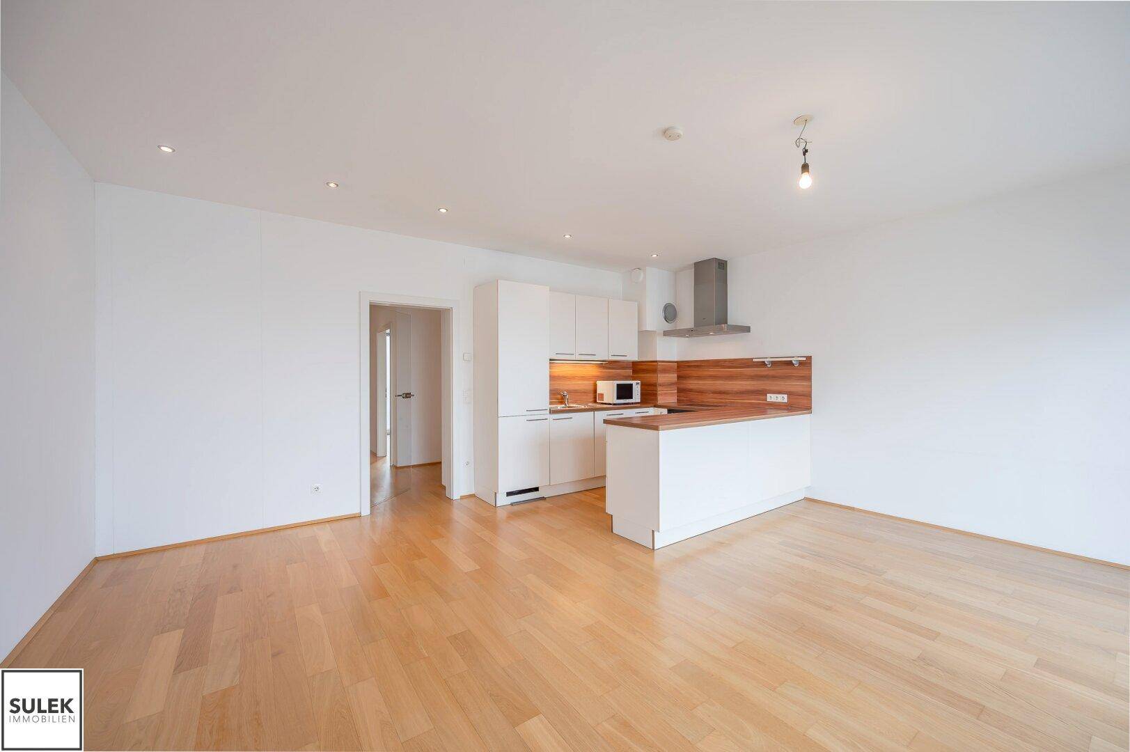 Offener Wohnbereich mit moderner Einbauküche und hellem Parkettboden, ideal für geselliges Beisammensein.