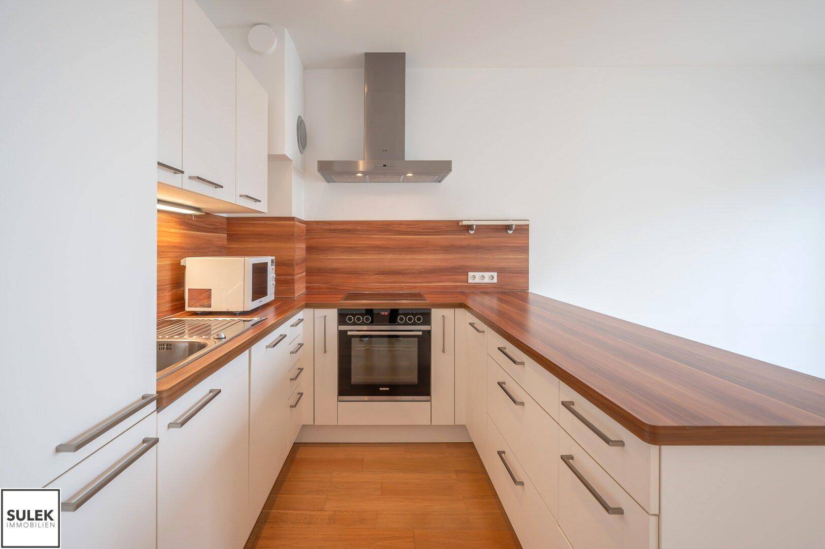 Gut ausgestattete Küche mit weißen Schränken, Holz-Arbeitsplatten und modernen Küchengeräten.