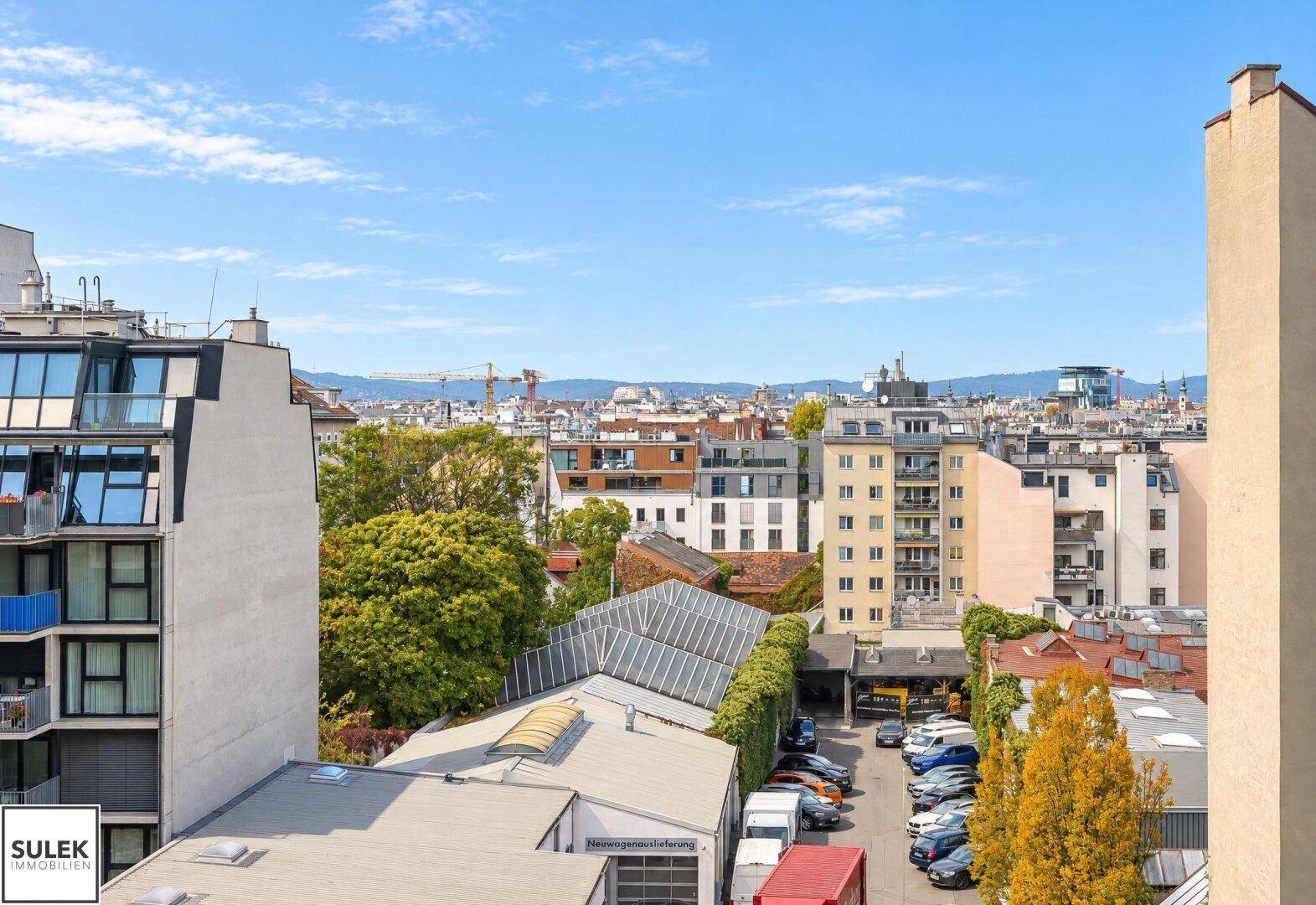 Panoramablick über die städtische Umgebung mit Dächern, Bäumen und einem Parkplatz.