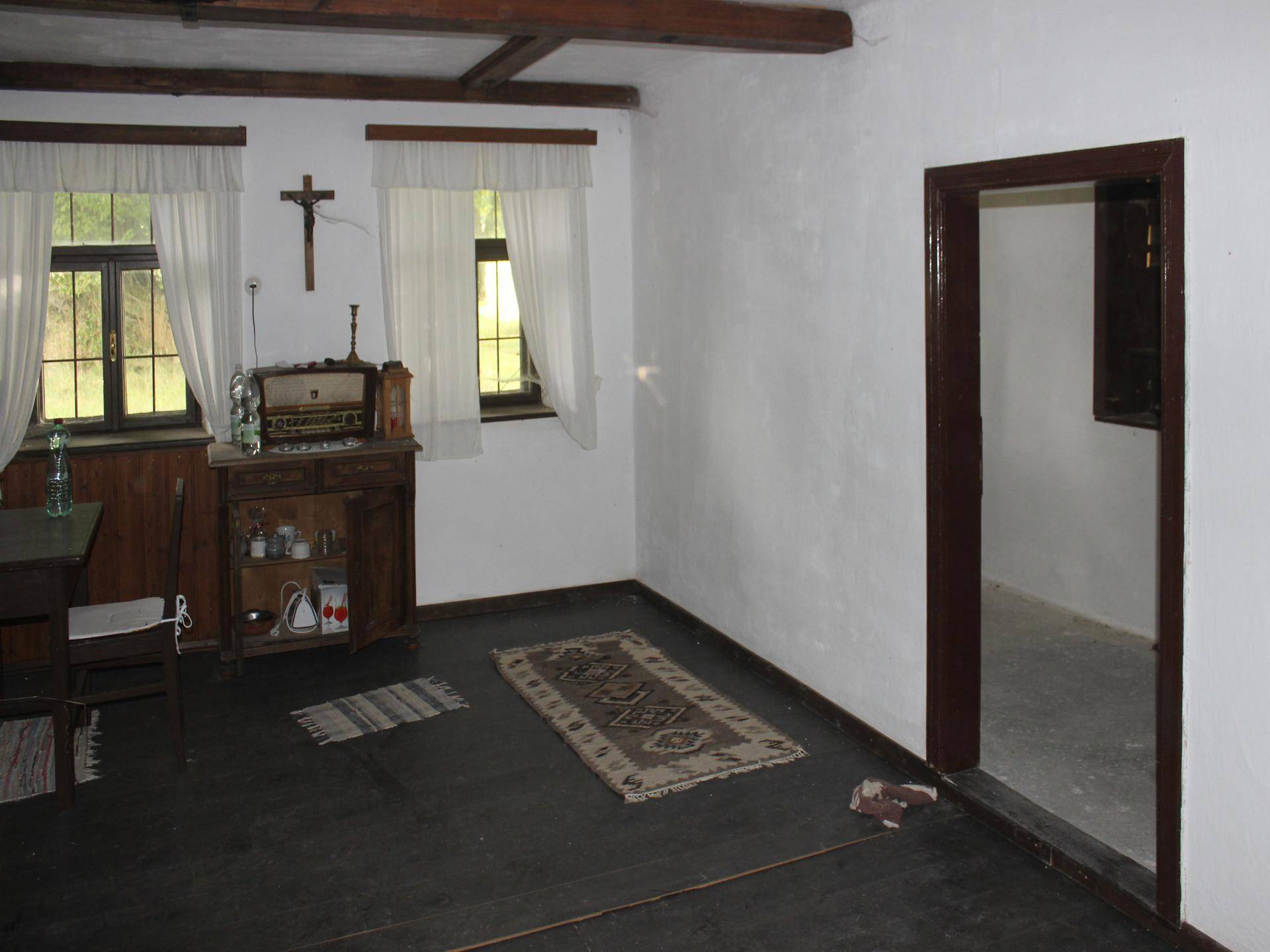 Gemütlicher Wohnraum mit Holzboden, zwei Fenstern und traditioneller Dekoration.