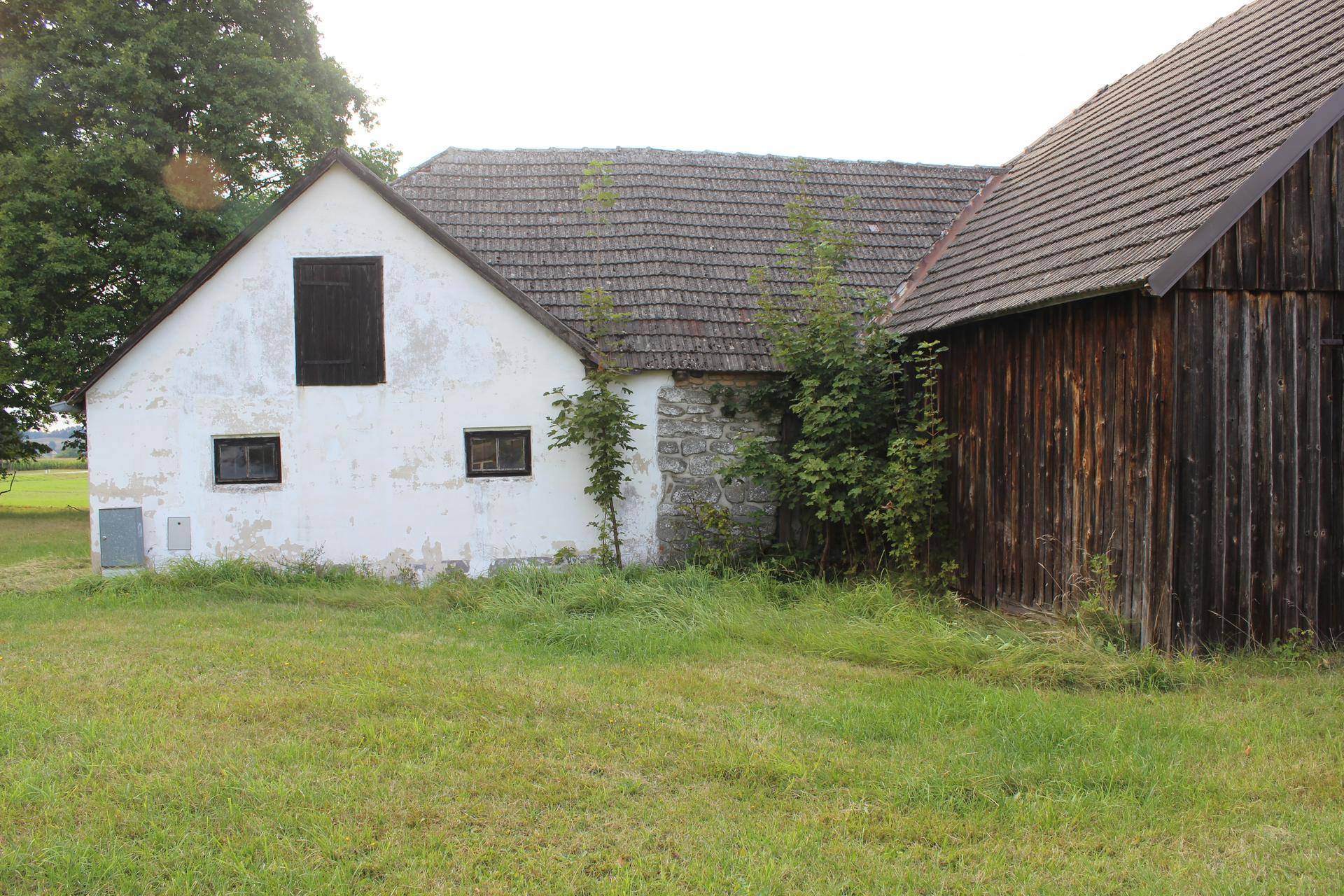 Rückansicht eines ländlichen Gebäudes mit weißer Fassade und angrenzender Holzscheune.