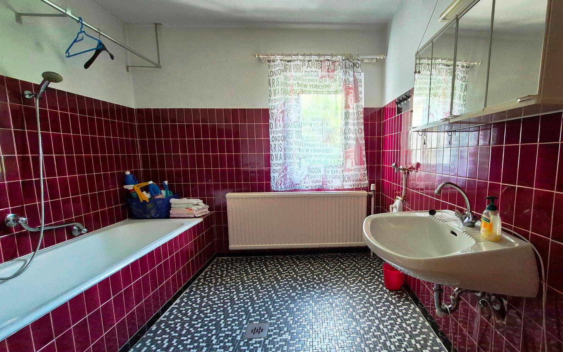 Badezimmer mit roten Fliesen, Badewanne und Waschbecken, im Stil der 80er Jahre.