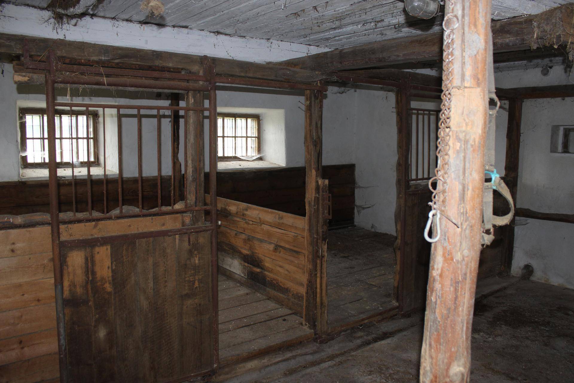 Innenansicht eines Stalls mit Holzwänden, Gitterfenstern und rustikalen Elementen.
