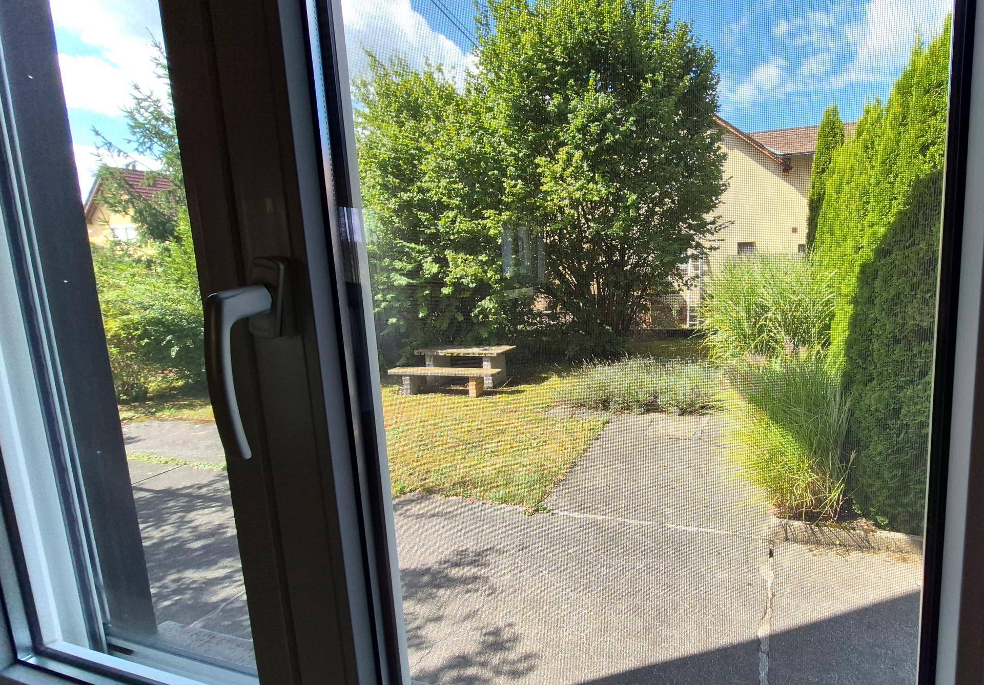 Blick aus dem Fenster auf den gepflegten Gartenbereich mit Sitzbank und viel Grün.