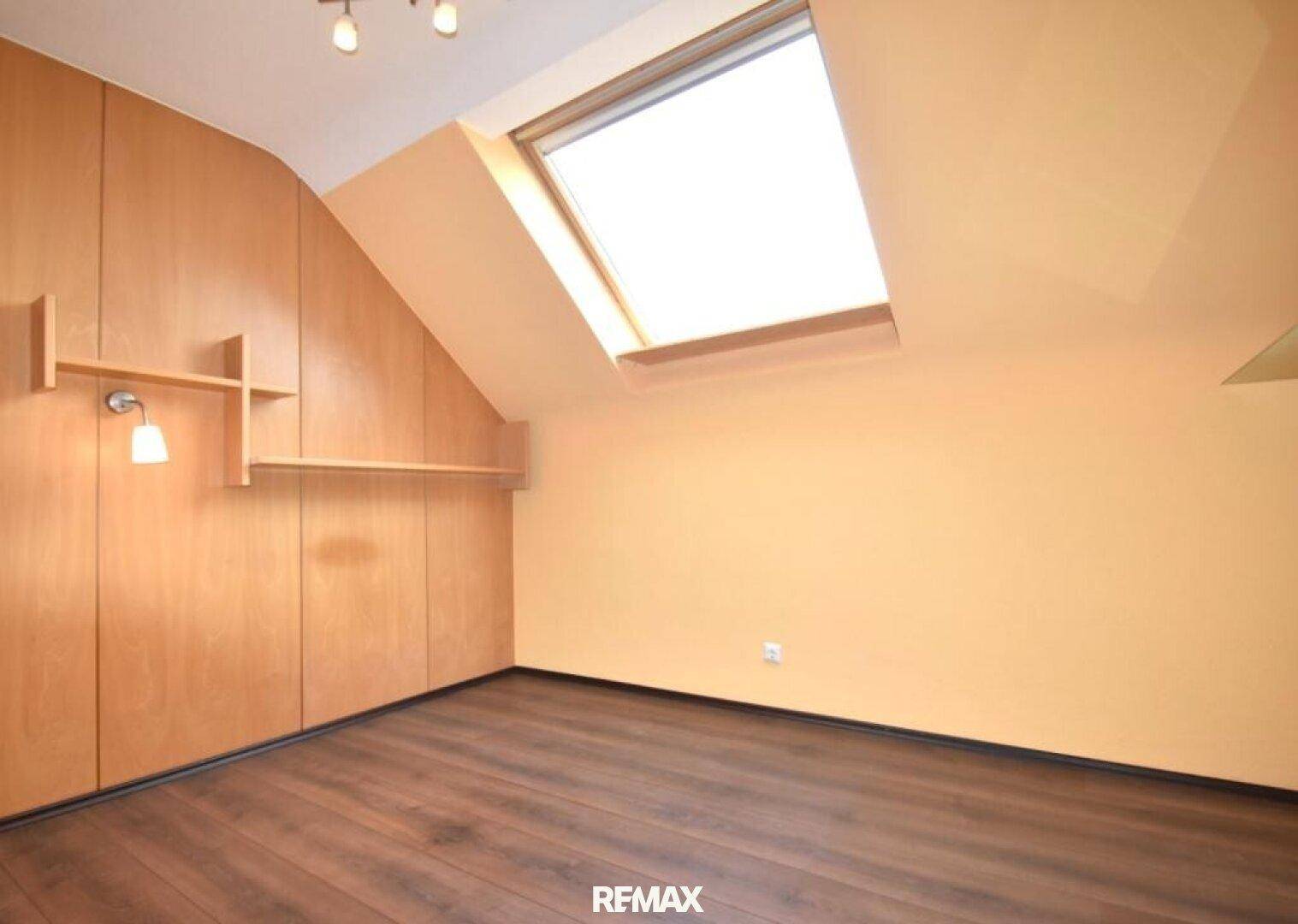 Helles Schlafzimmer mit großem Dachfenster, Dachschräge und Holzwänden.