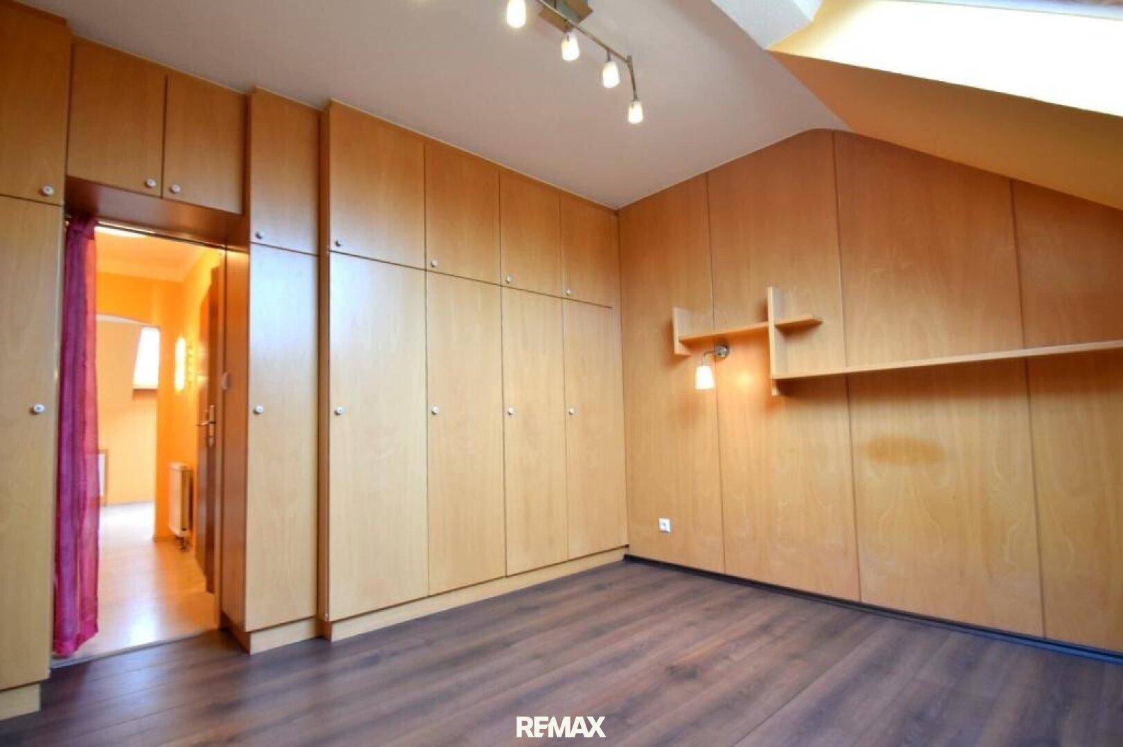 Schlafzimmer mit maßgefertigten Holzschränken, Dachschräge und dunklem Laminatboden.