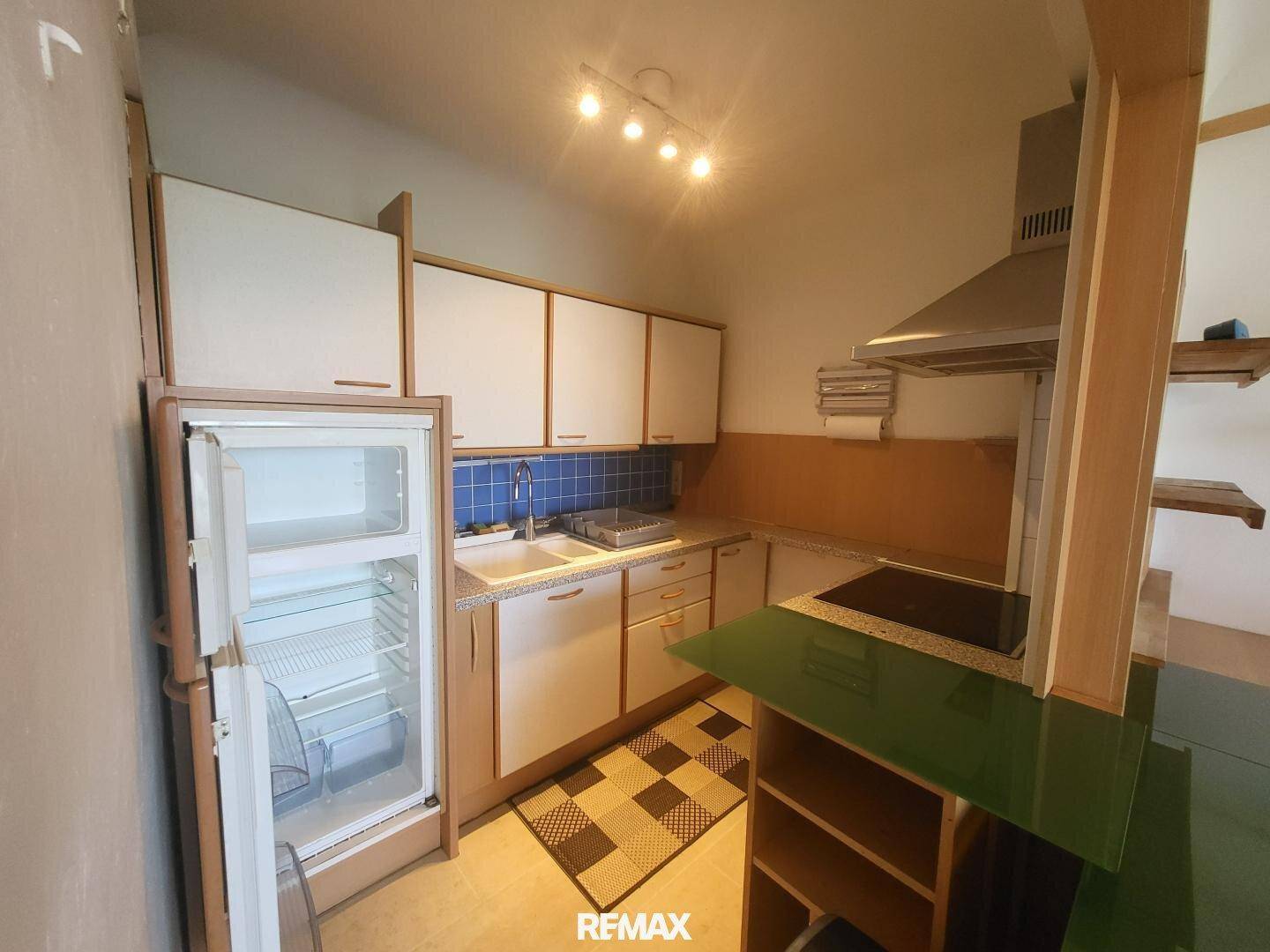 Funktionale Küche mit weißen Schränken, blauen Fliesen und integriertem Kühlschrank.