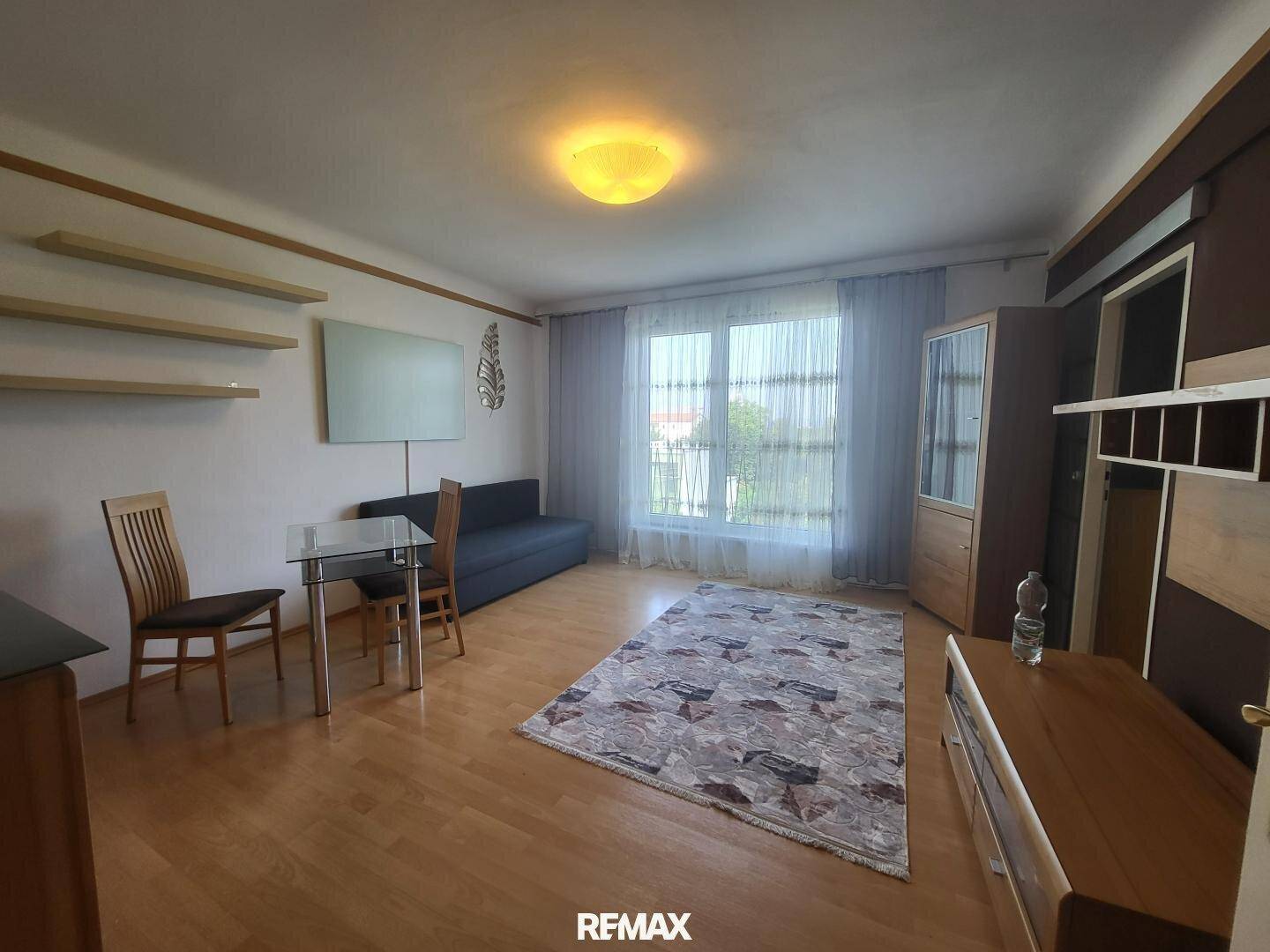 Helles Wohnzimmer mit Holzboden, Sofa und großem Fenster mit Vorhängen.