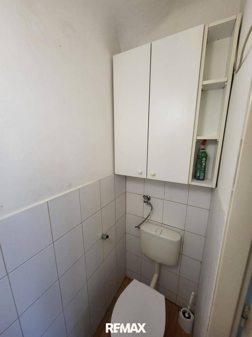 Separates WC mit weißer Toilette, Fliesen und Hängeschränken.