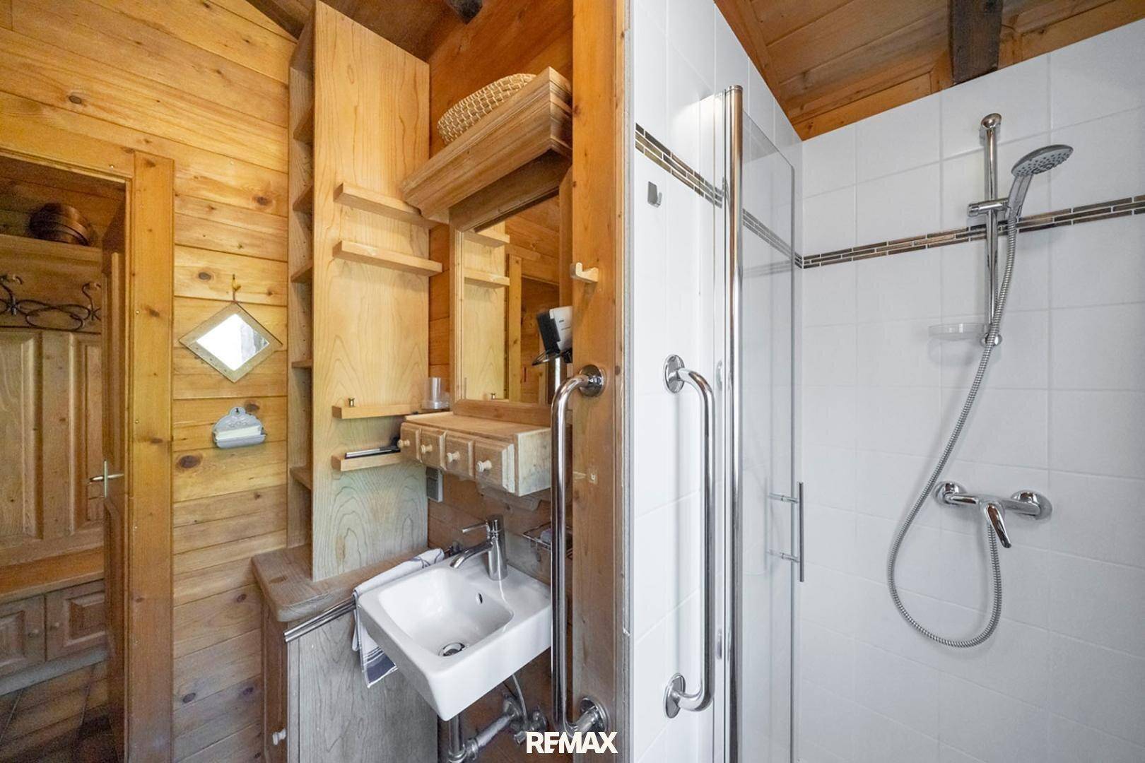Badezimmer mit Duschkabine, Holzvertäfelung und praktischen Ablagen.