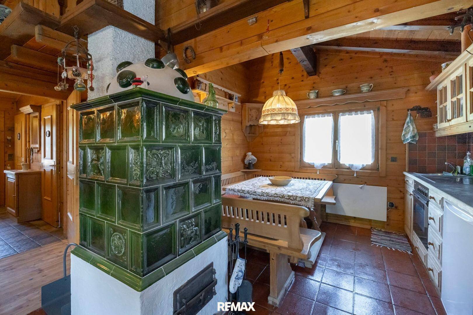 Traditionelle Küche mit grünem Kachelofen, Holzbänken und rustikalem Esstisch.