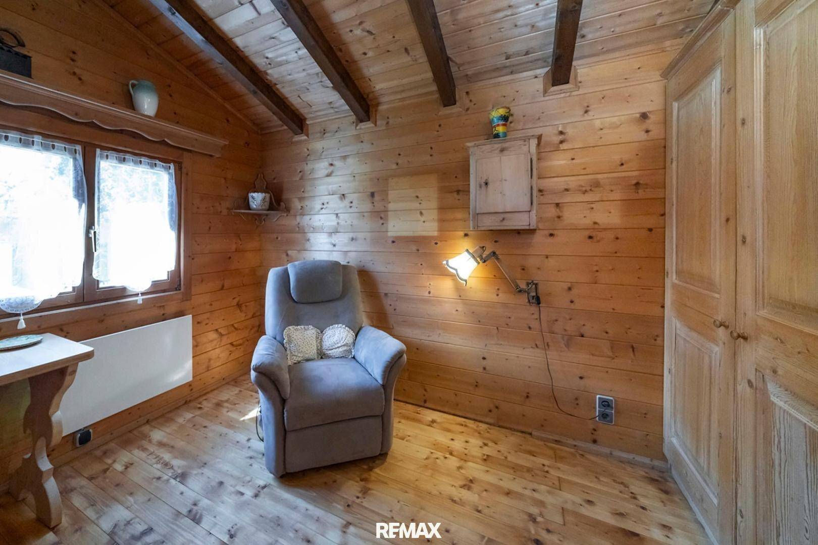 Gemütliches Schlafzimmer mit Holzvertäfelung, Holzboden und einem bequemen Sessel.