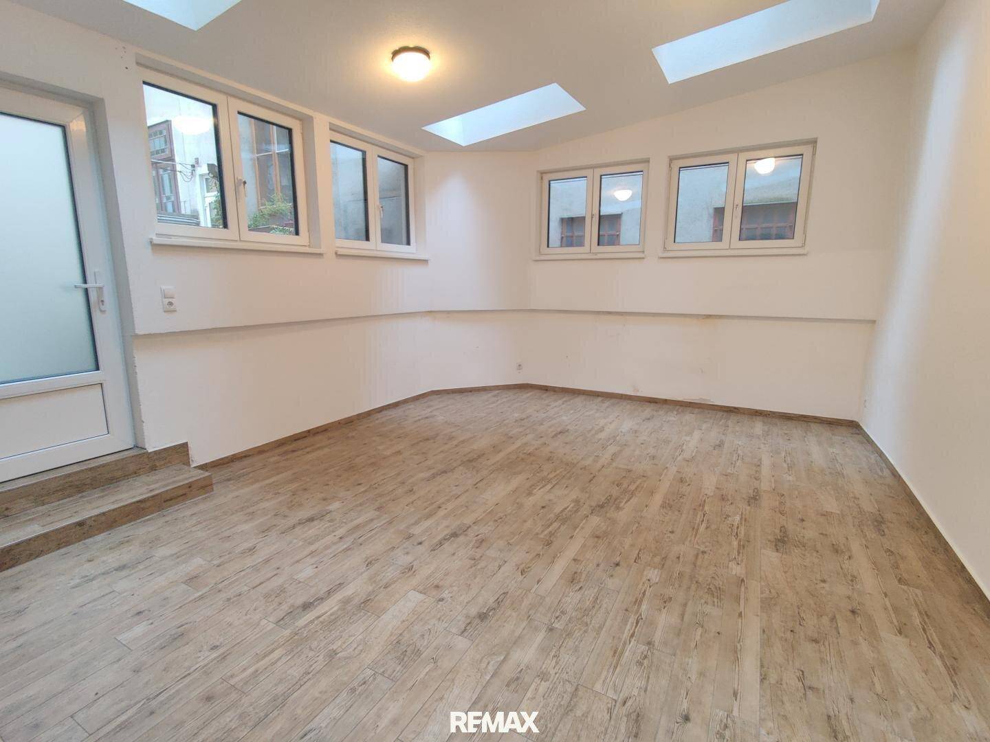 Geräumiges Zimmer mit Holzoptik-Boden, vielen Fenstern und Dachfenstern für viel Helligkeit.