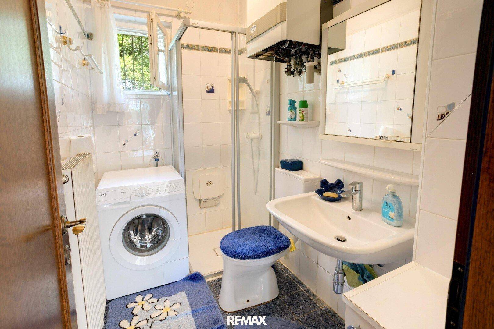Kleines Badezimmer mit Dusche, Waschbecken, WC und Waschmaschine.