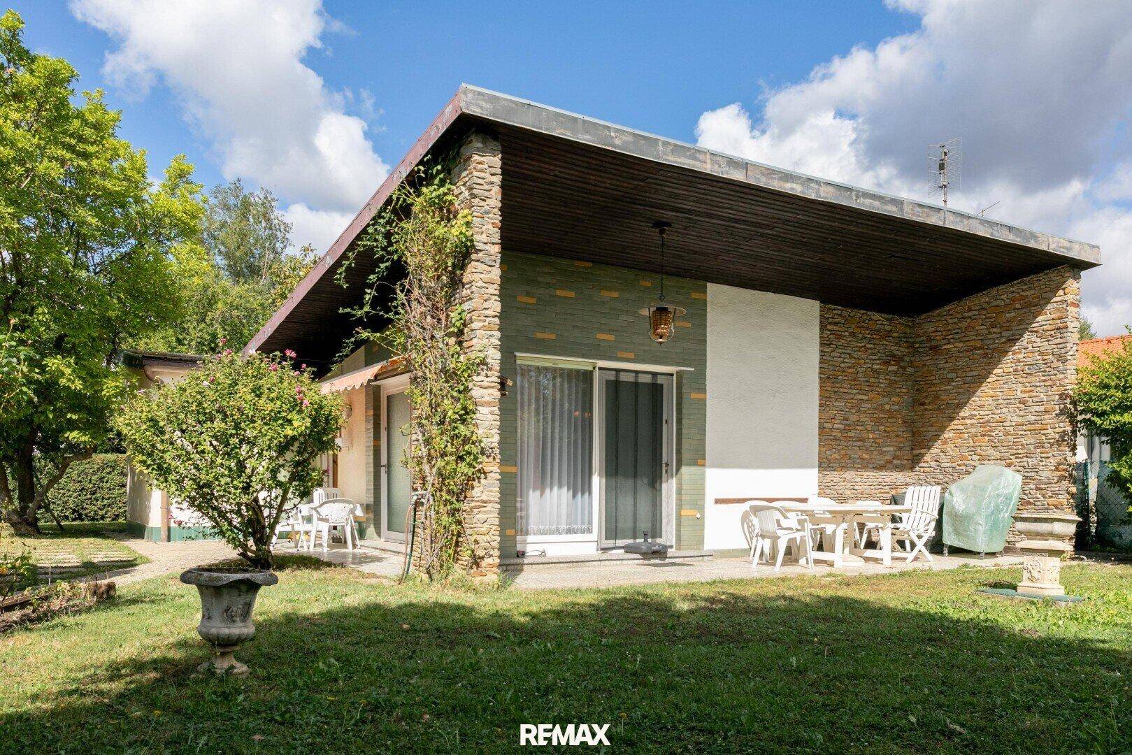 Rückseite des Hauses mit gepflasterter Terrasse, Gartenmöbeln und Steinverkleidung.