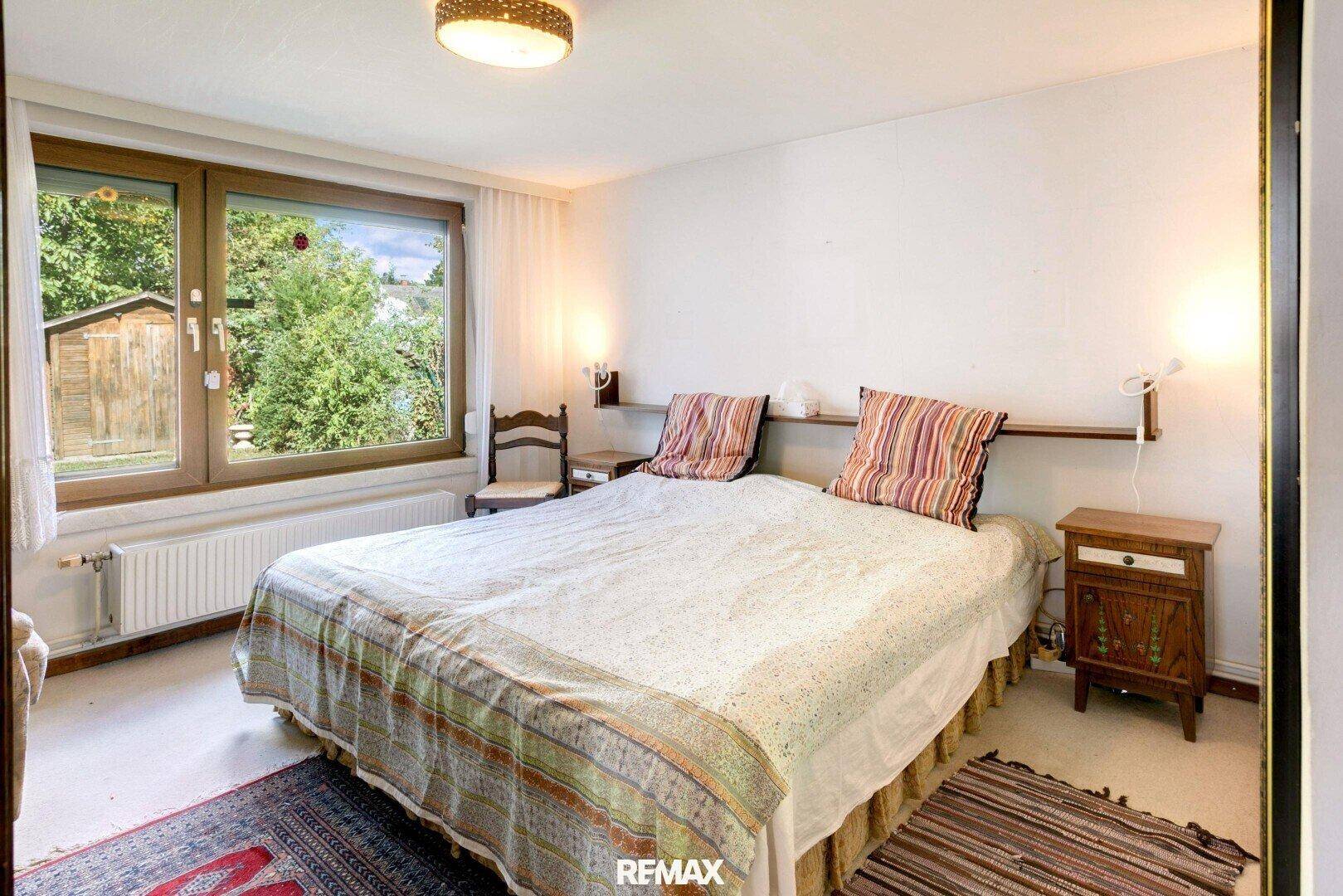 Gemütliches Schlafzimmer mit Doppelbett, Teppichboden und Blick in den Garten.