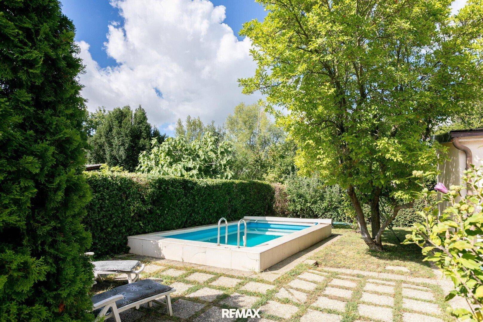 Eingebetteter Swimmingpool im Gartenbereich, umgeben von Hecken und Bäumen.