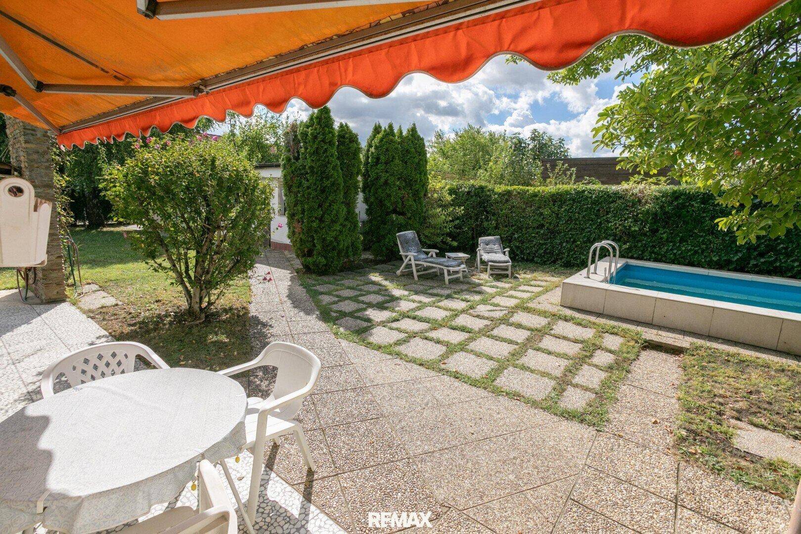 Sonniger Terrassenbereich mit Gartenmöbeln, Markise und Blick auf den Pool.