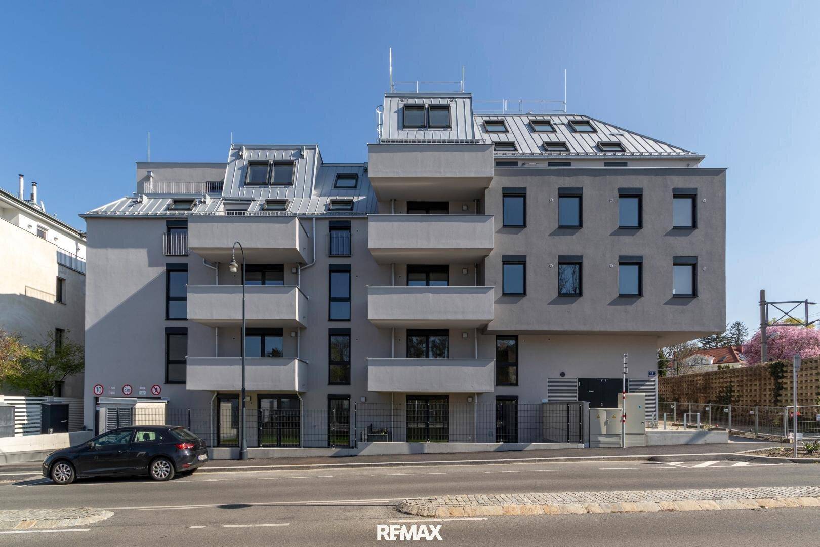 Neubau-Wohngebäude mit moderner Fassade, Balkonen und Mansarddach an einer städtischen Straße.