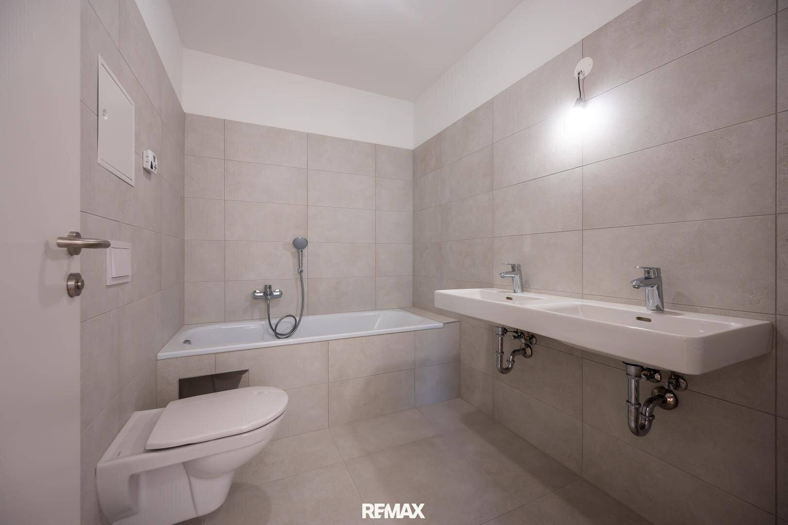 Modernes Badezimmer mit hellgrauen Fliesen, Doppelwaschbecken und Badewanne, in gutem Zustand.