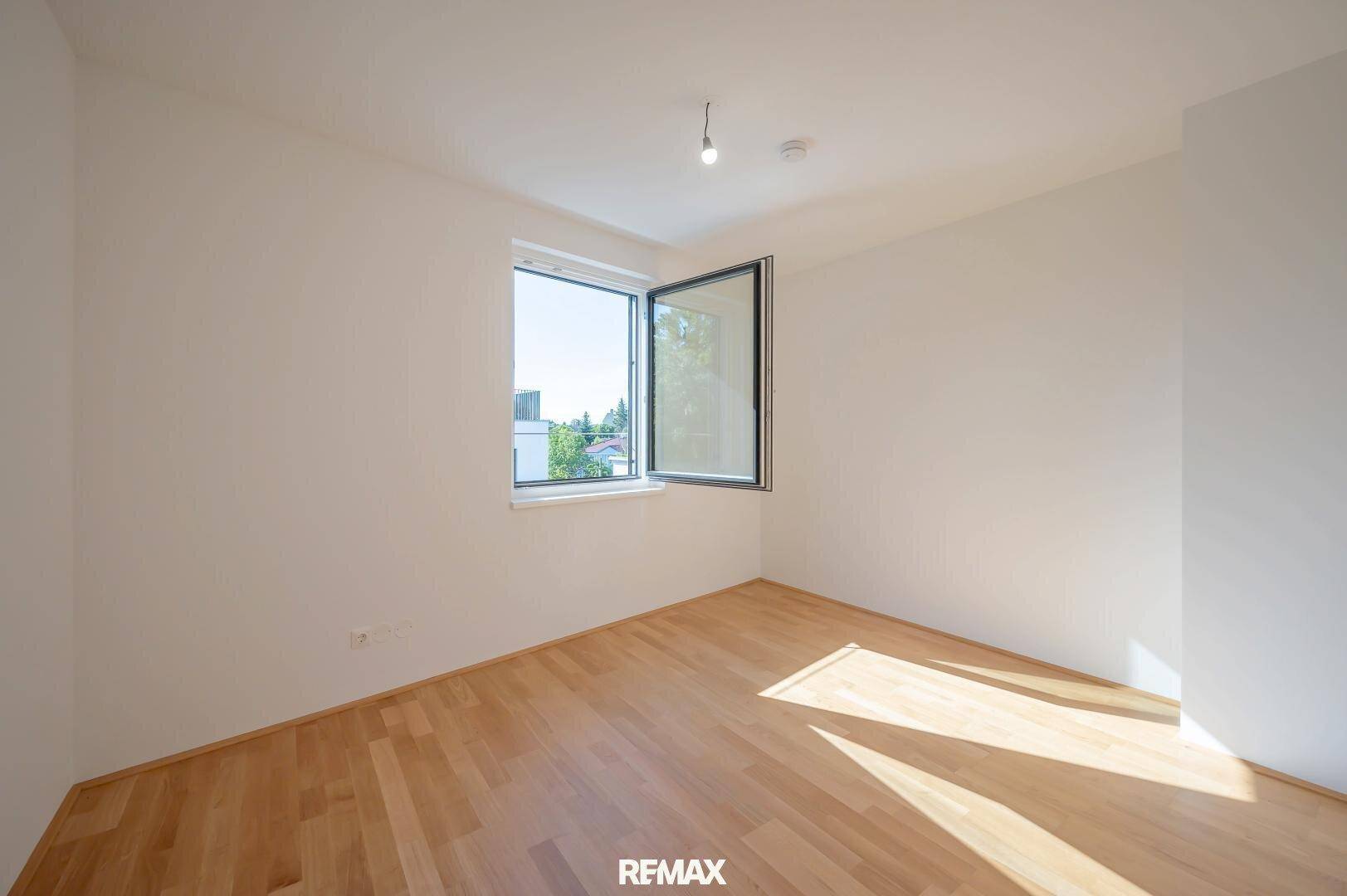 Helles Schlafzimmer mit Holzboden und einem großen Fenster, das viel Tageslicht hereinlässt.