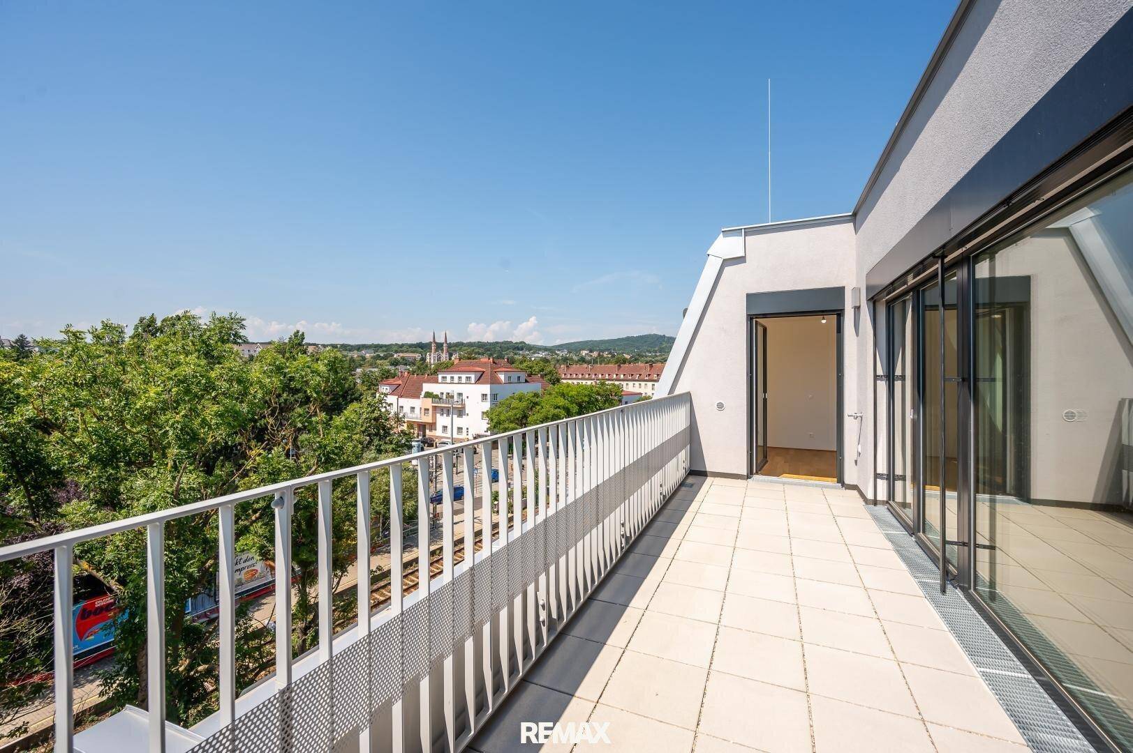 Große, geflieste Dachterrasse mit Metallgeländer und weitem Blick über die Stadt und grüne Umgebung.