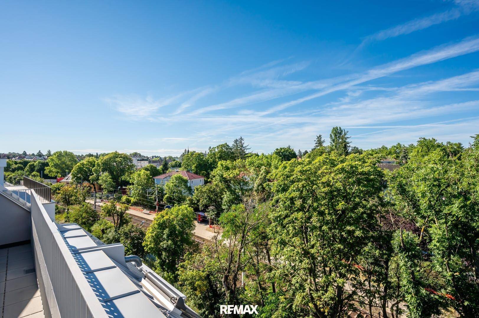 Panoramablick über eine grüne Wohngegend mit vielen Bäumen und Häusern unter blauem Himmel.
