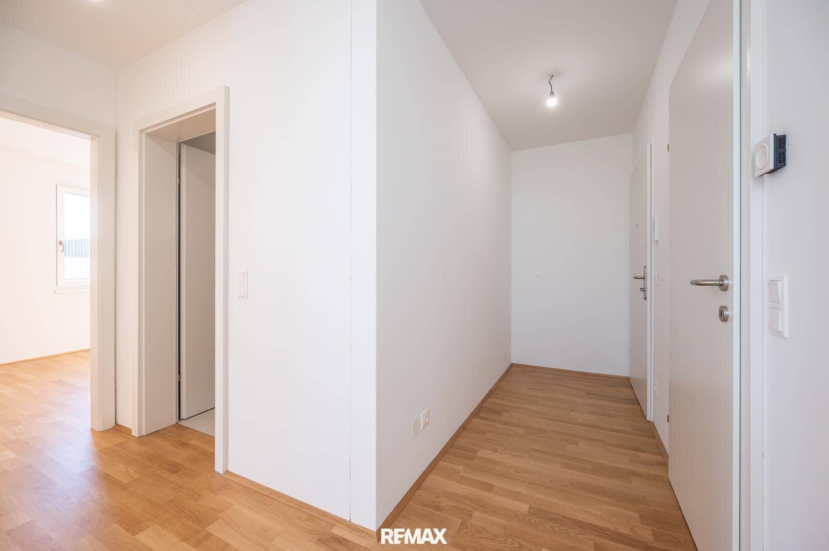 Heller Flur mit Holzboden und weißen Wänden, der zu verschiedenen Räumen führt.