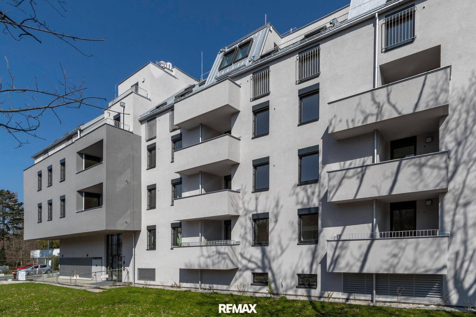 Moderne Wohnanlage mit mehreren Balkonen und großen Fenstern, umgeben von Grünflächen.