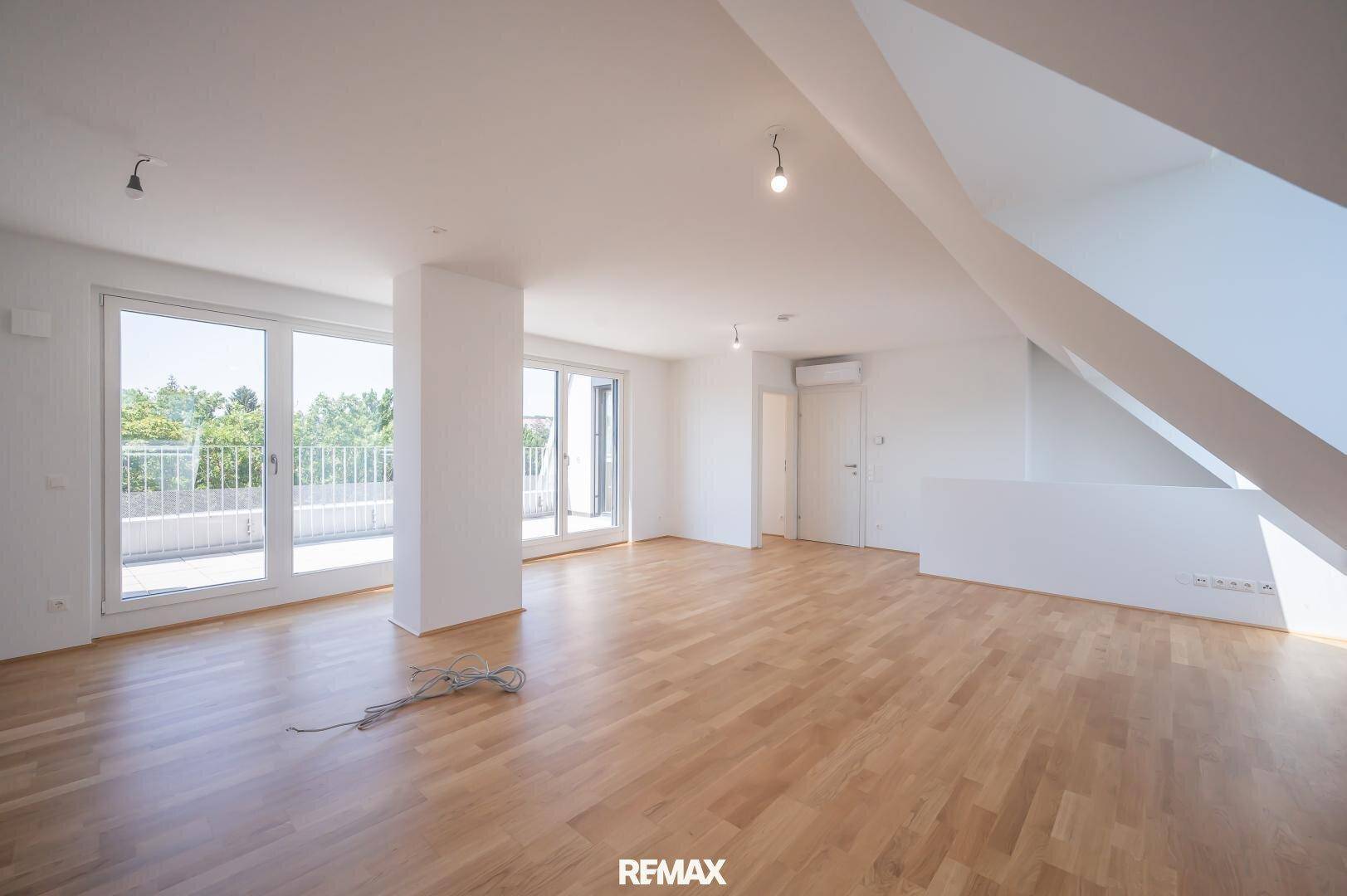 Offener Wohnbereich mit Holzboden, großen Fenstern und Zugang zur Terrasse, ideal für helle Räume.