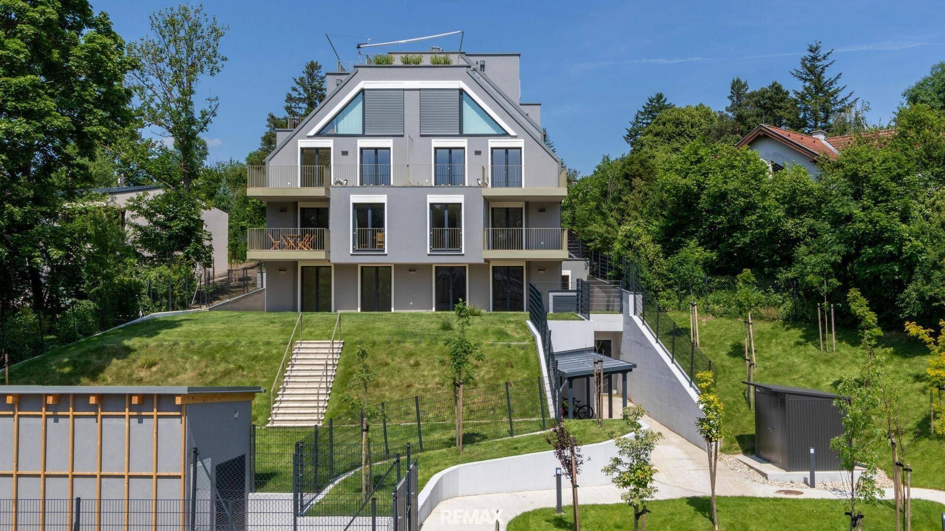 Modernes Mehrfamilienhaus mit Terrassen und Balkonen in grüner Hanglage und Tiefgaragenzufahrt.
