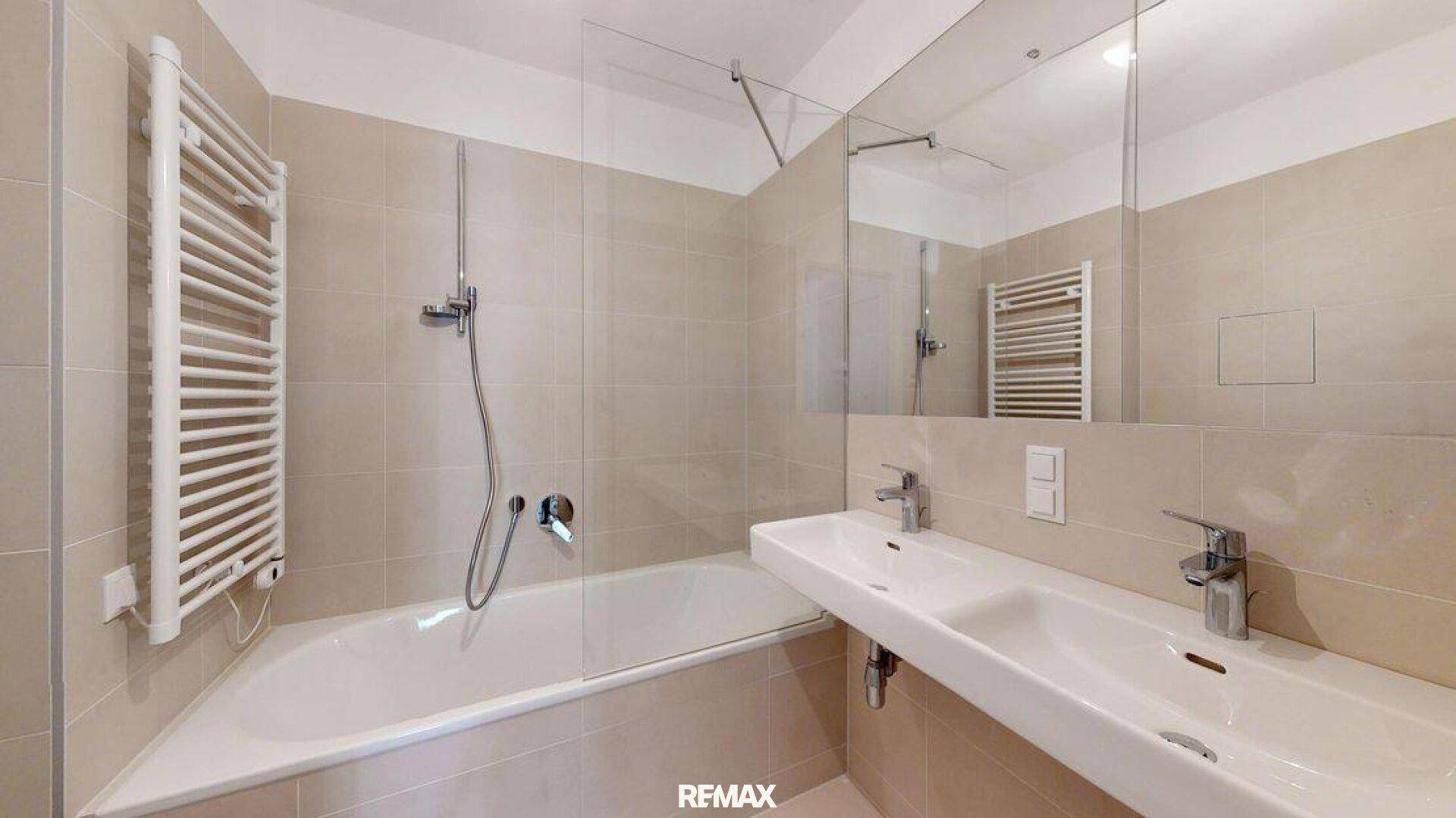 Modernes Badezimmer mit beigefarbenen Fliesen, Badewanne und einem praktischen Doppelwaschbecken.