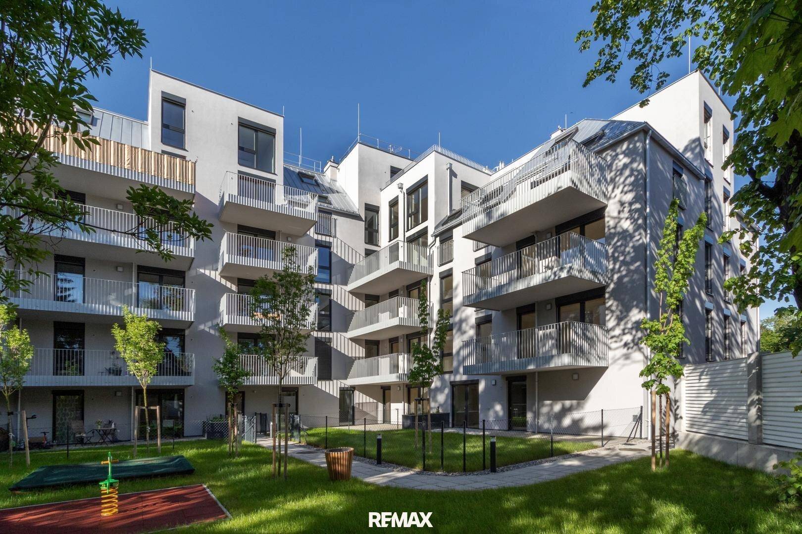 Moderne Wohnanlage mit mehreren Balkonen und einem gemeinschaftlichen Gartenbereich mit Spielplatz.